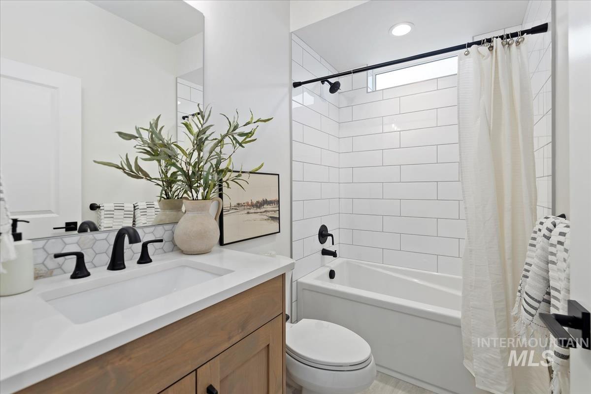 Full bathroom featuring shower / tub combo with curtain, vanity, and decorative backsplash