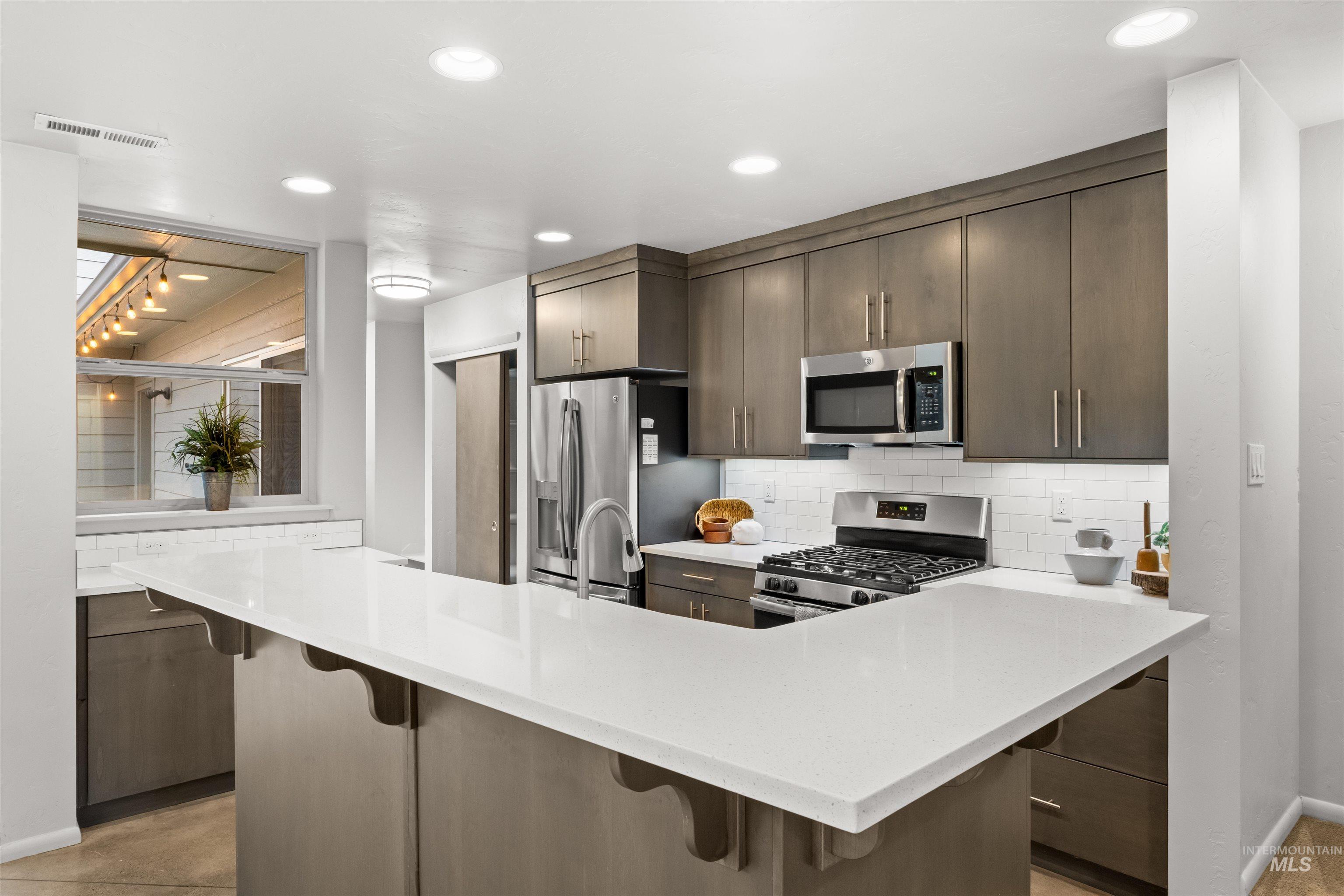 Kitchen featuring appliances with stainless steel finishes, dark grey cabinetry, subway tile backsplash, a breakfast bar, and recessed lighting