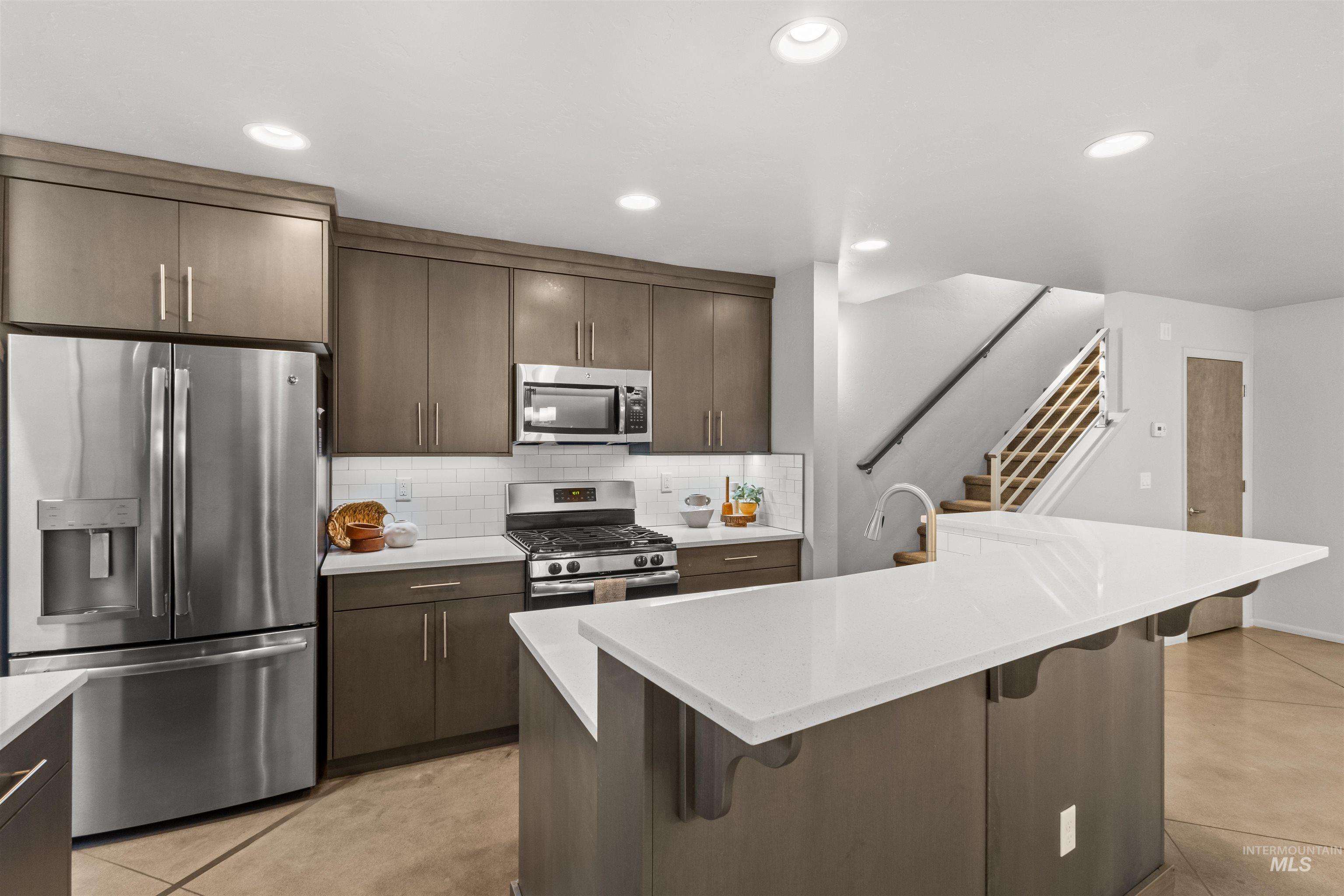 Kitchen featuring stainless steel appliances, a kitchen breakfast bar, subway tile backsplash, an island with sink, and light quartz countertops