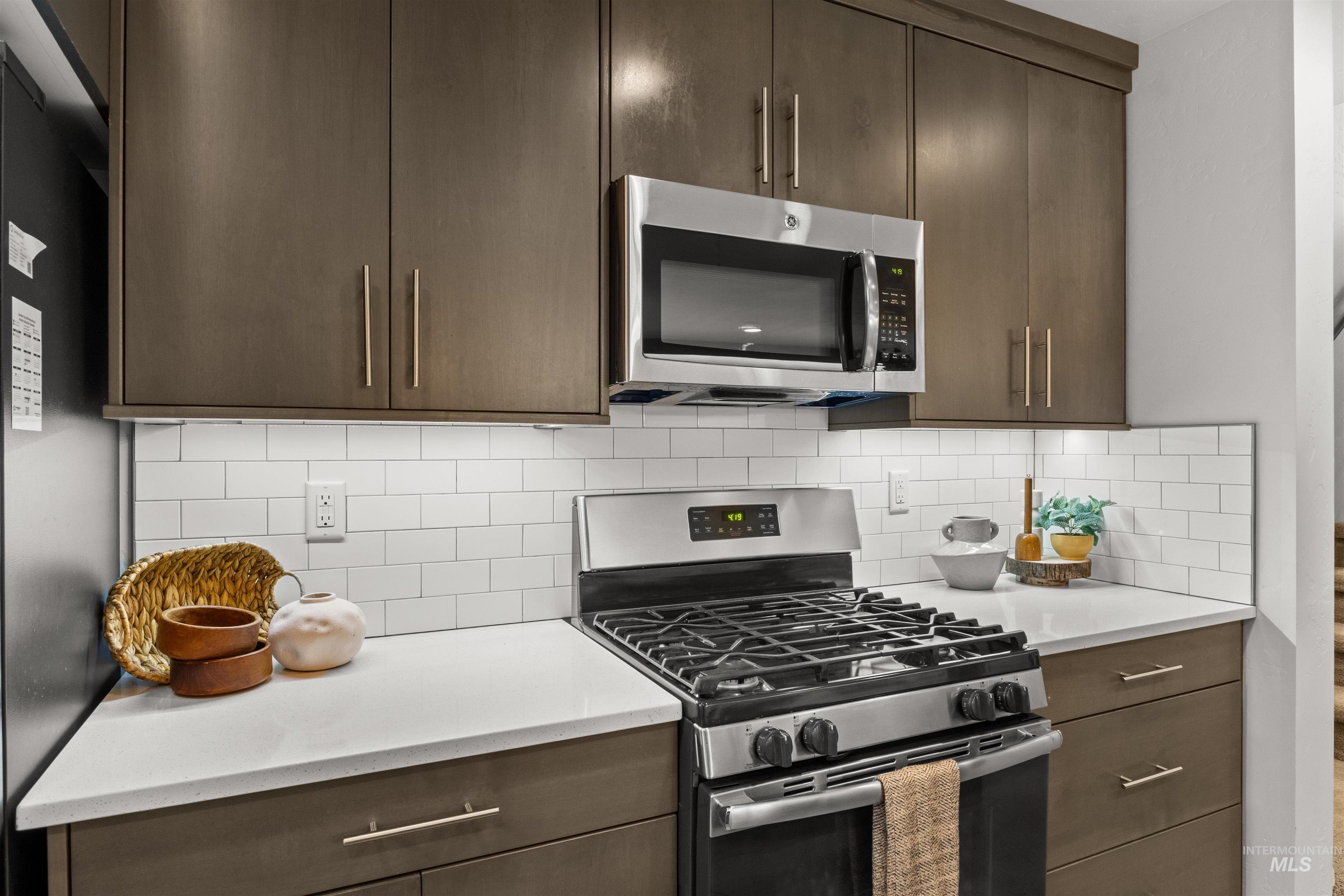 Kitchen featuring appliances with stainless steel finishes, dark grey cabinetry, subway tile backsplash, and light quartz countertops
