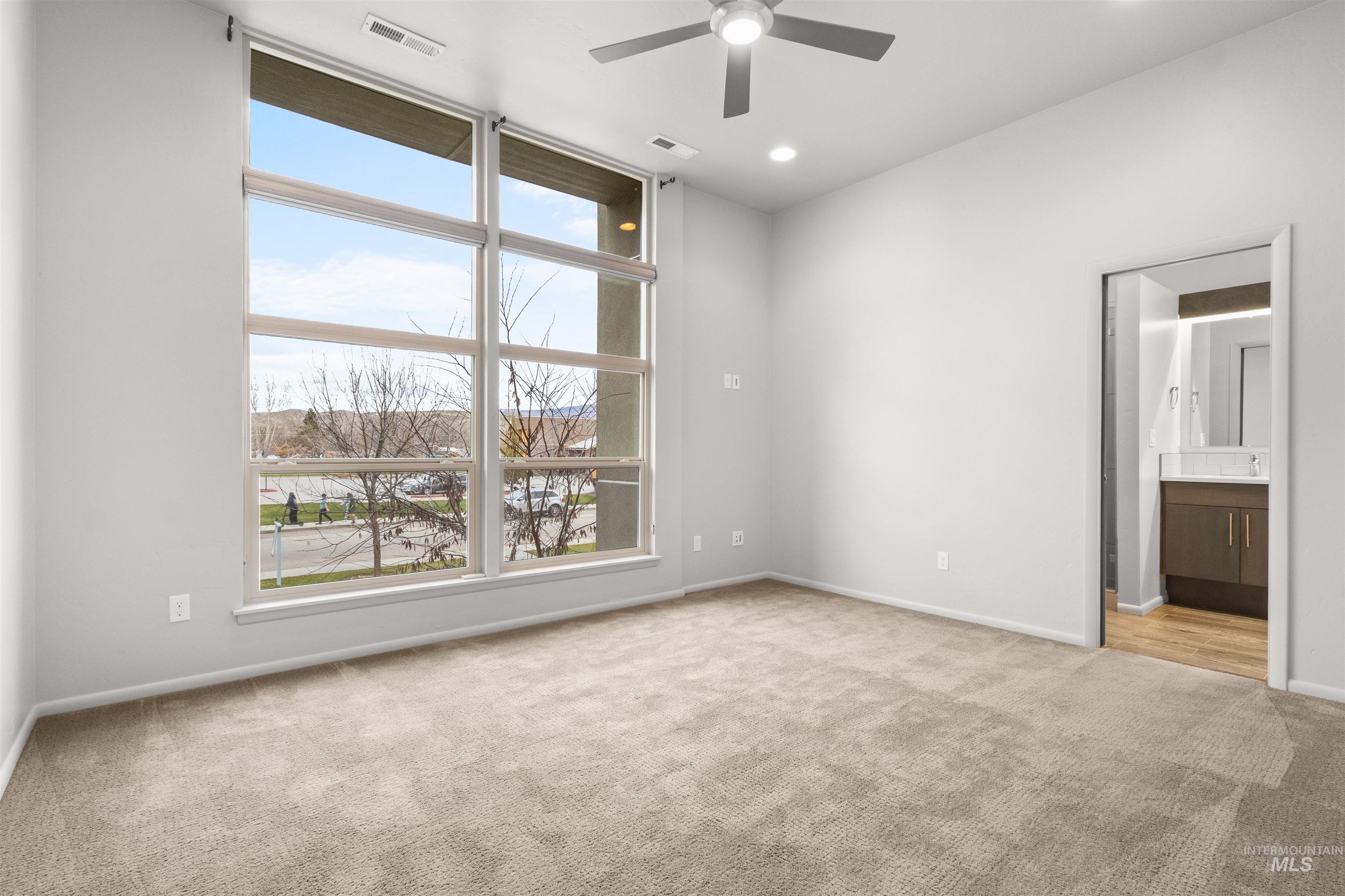 Expansive master bedroom with light colored carpet, 10-ft ceiling, large windows, and a ceiling fan