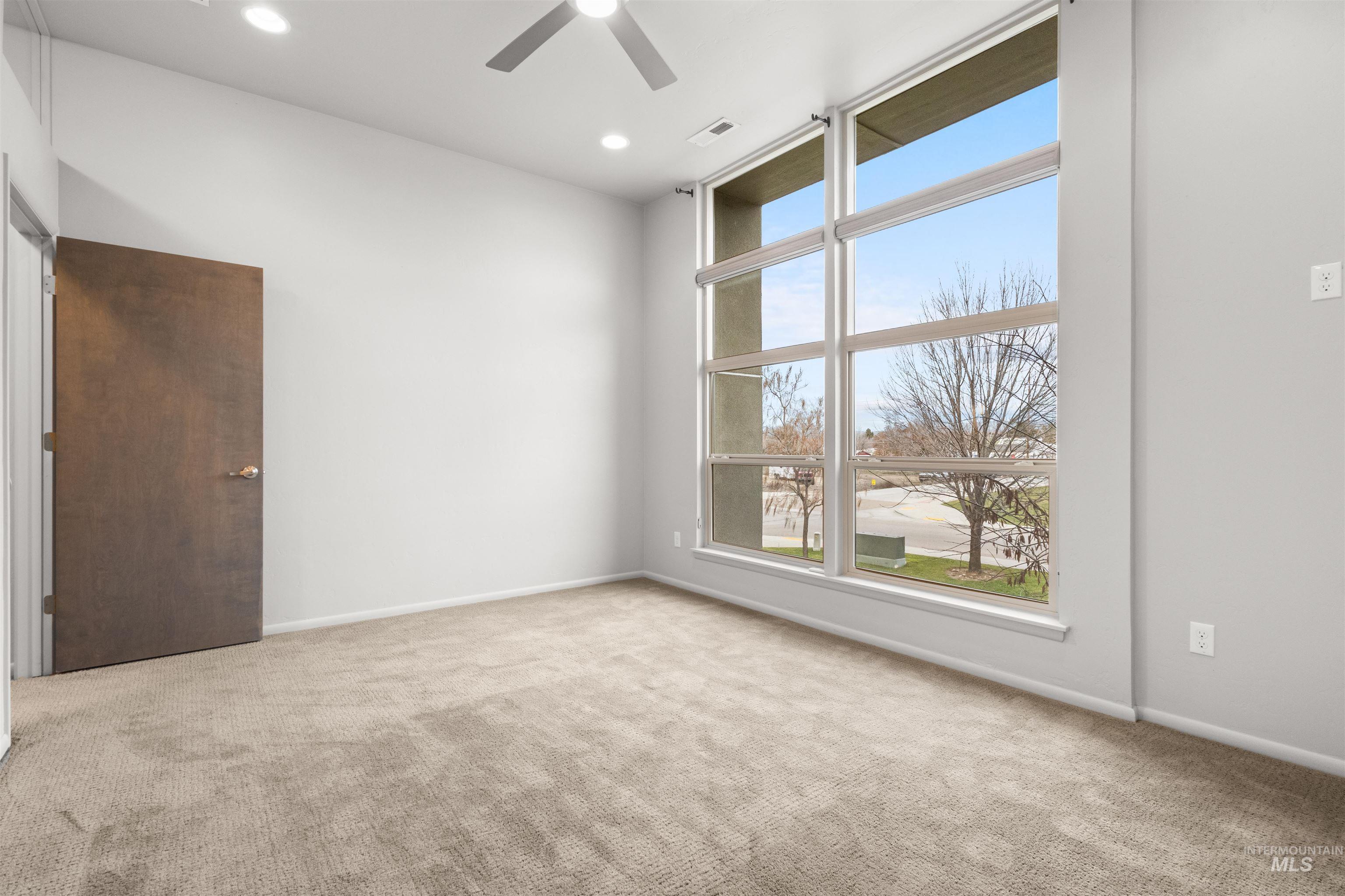Expansive master bedroom with light colored carpet, 10-ft ceiling, large windows, and a ceiling fan