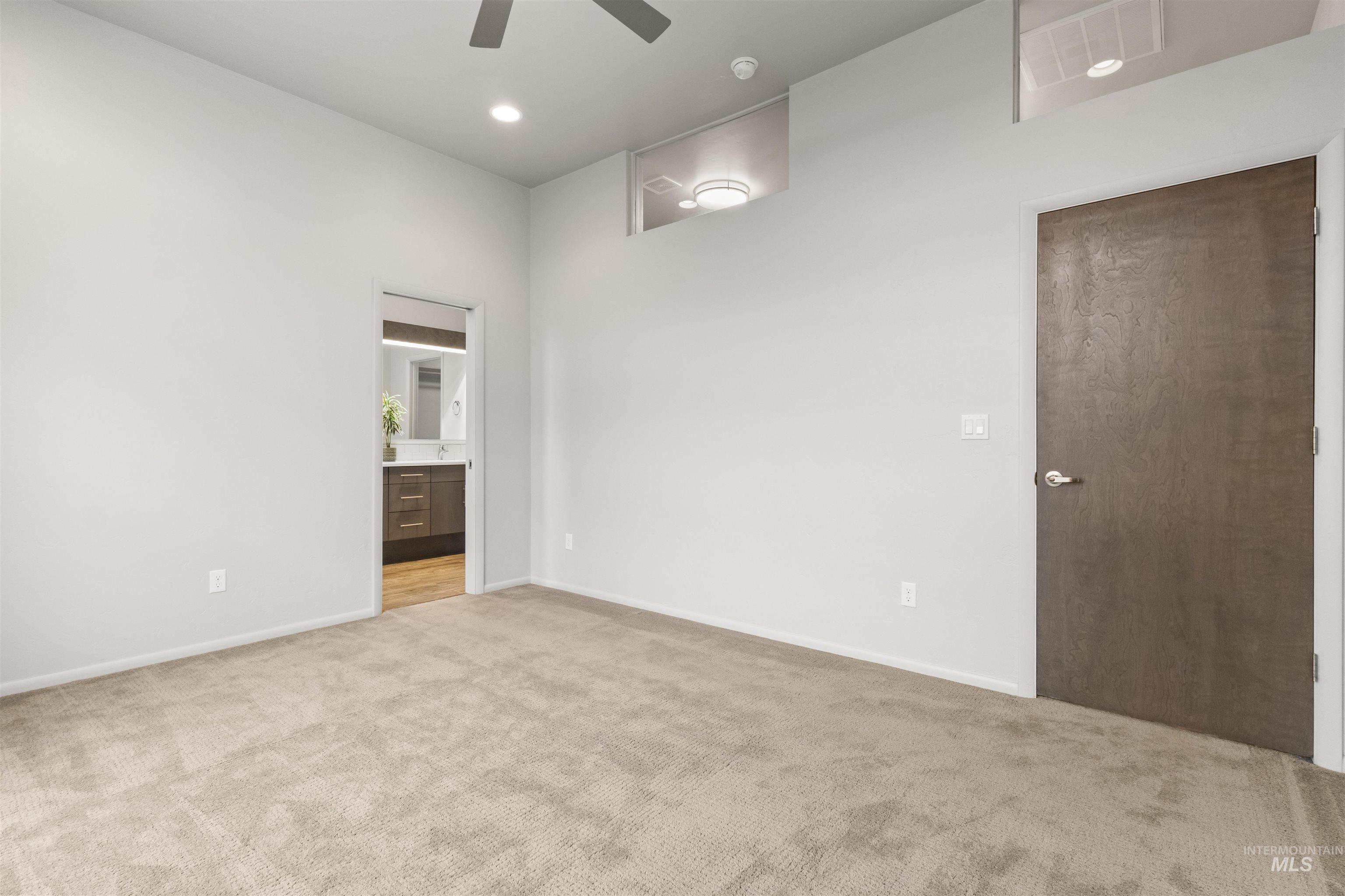 Expansive master bedroom featuring connected bathroom, light carpet, ceiling fan, and recessed lighting