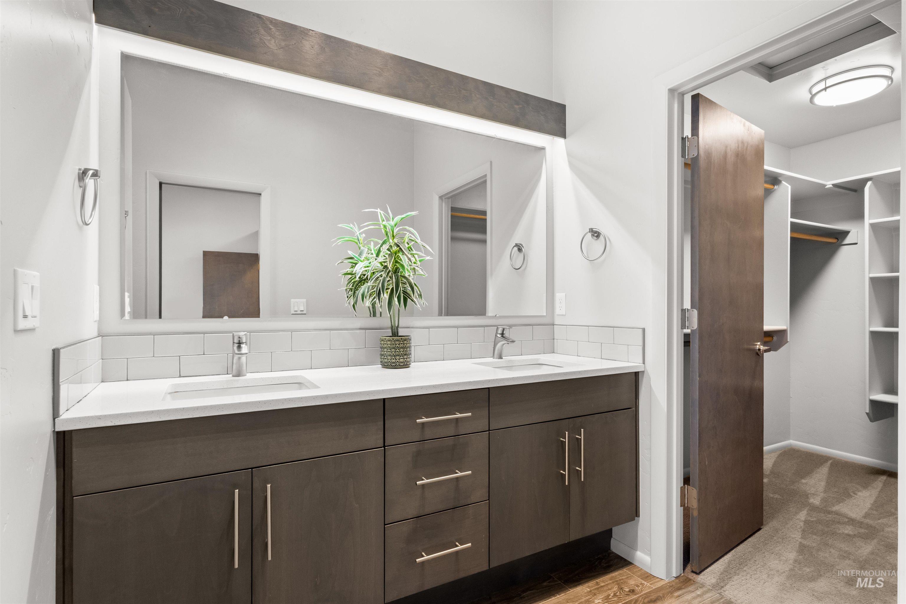 Full master bathroom featuring double vanity, a spacious closet, backsplash, and light wood-look tile plank floors