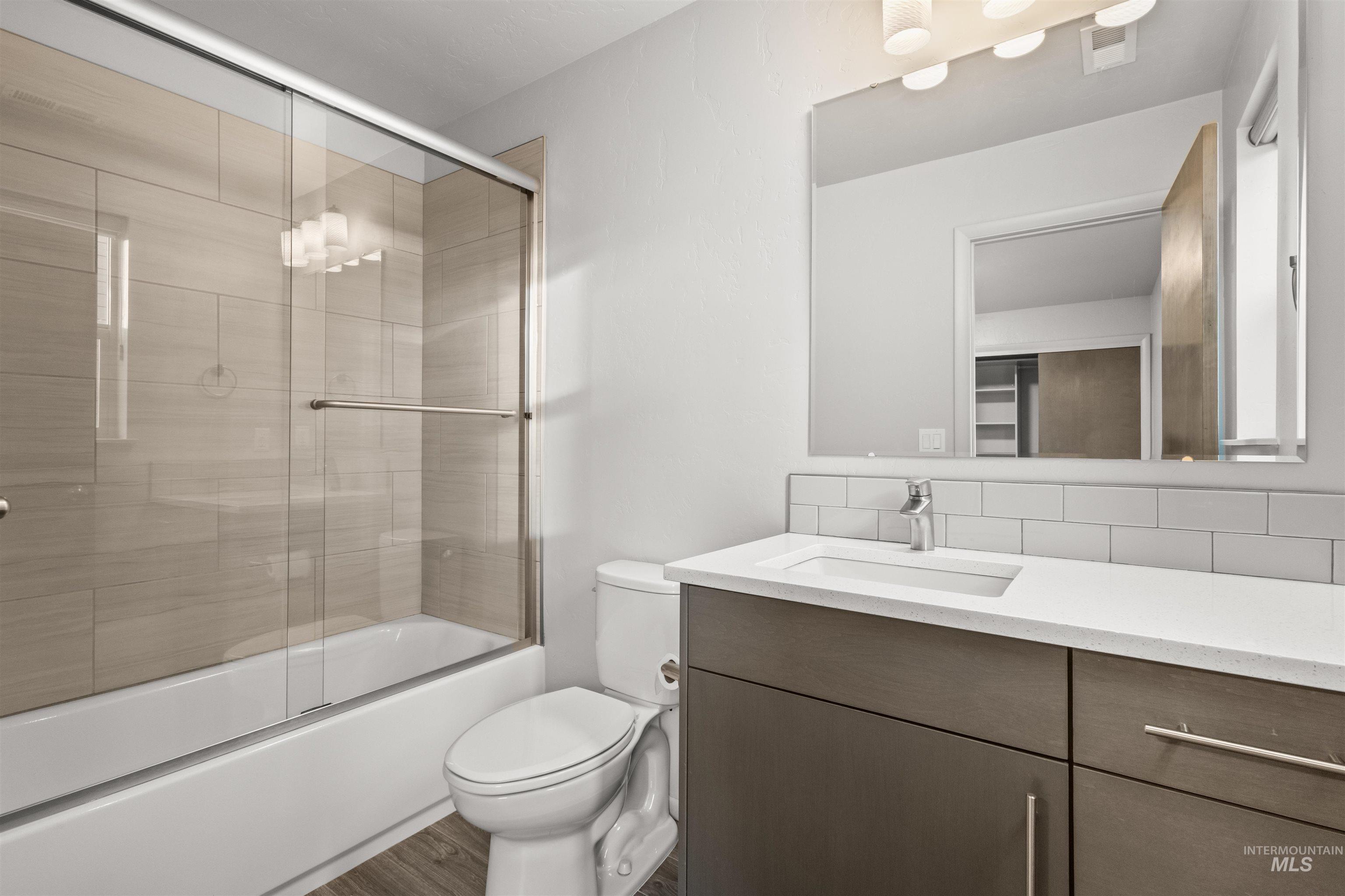 Bathroom attached to bedroom featuring vanity, combined bath / shower with glass door, and wood-look tile plank flooring