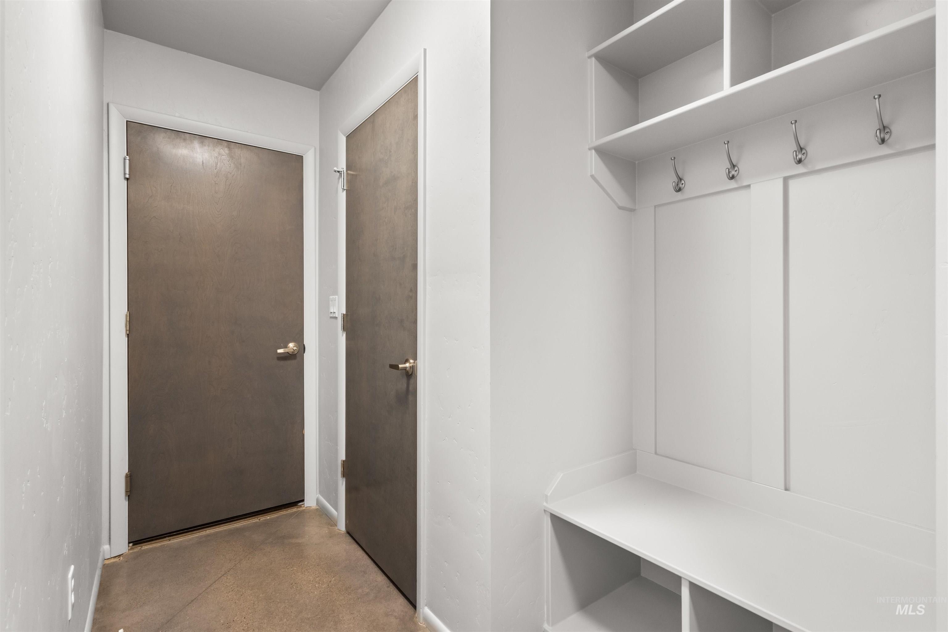 Mudroom hallway featuring concrete flooring, built-in bench, storage cubbies, and closet.