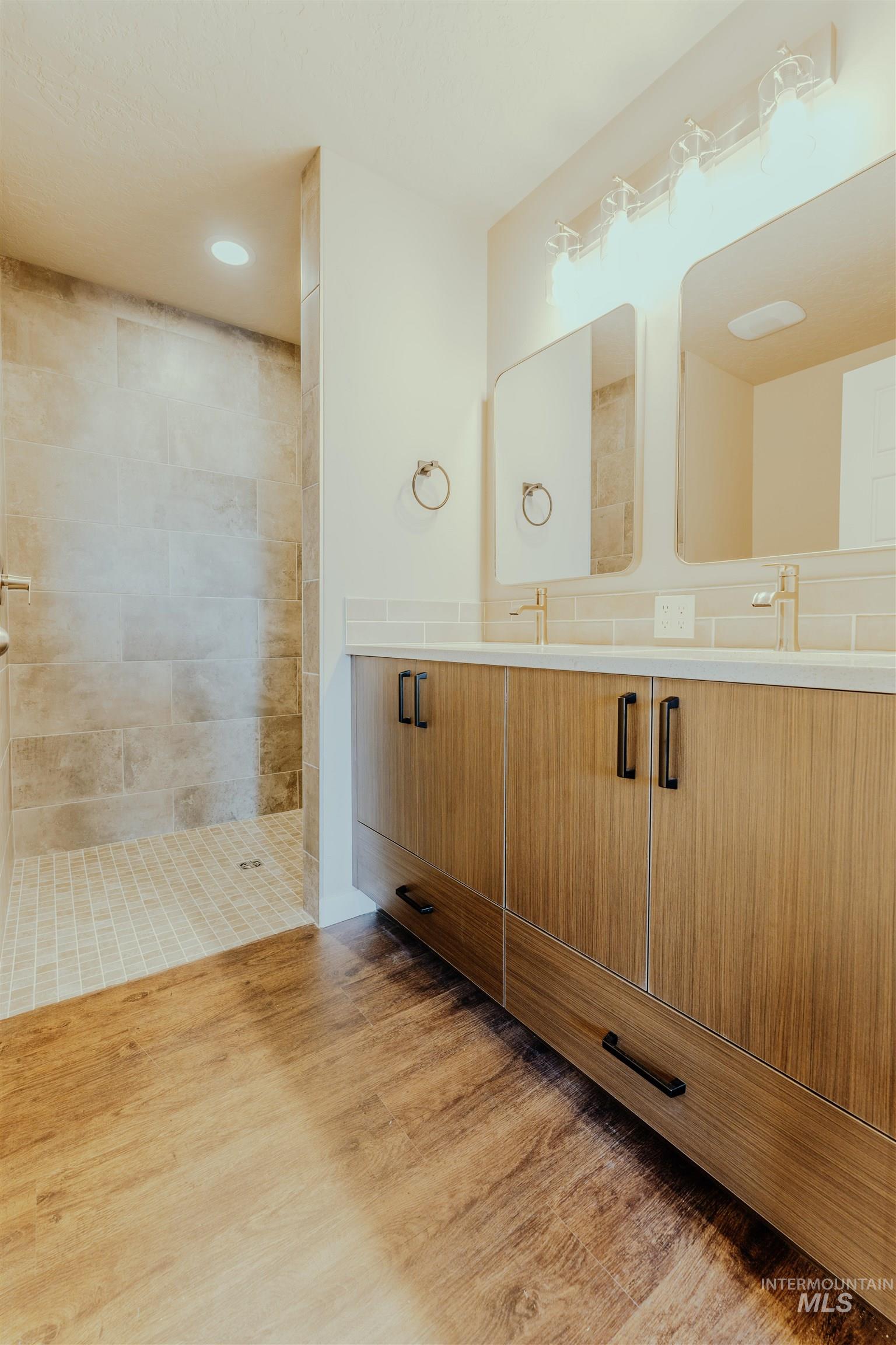 Bathroom featuring double vanity, light wood-type flooring, walk in shower, and recessed lighting