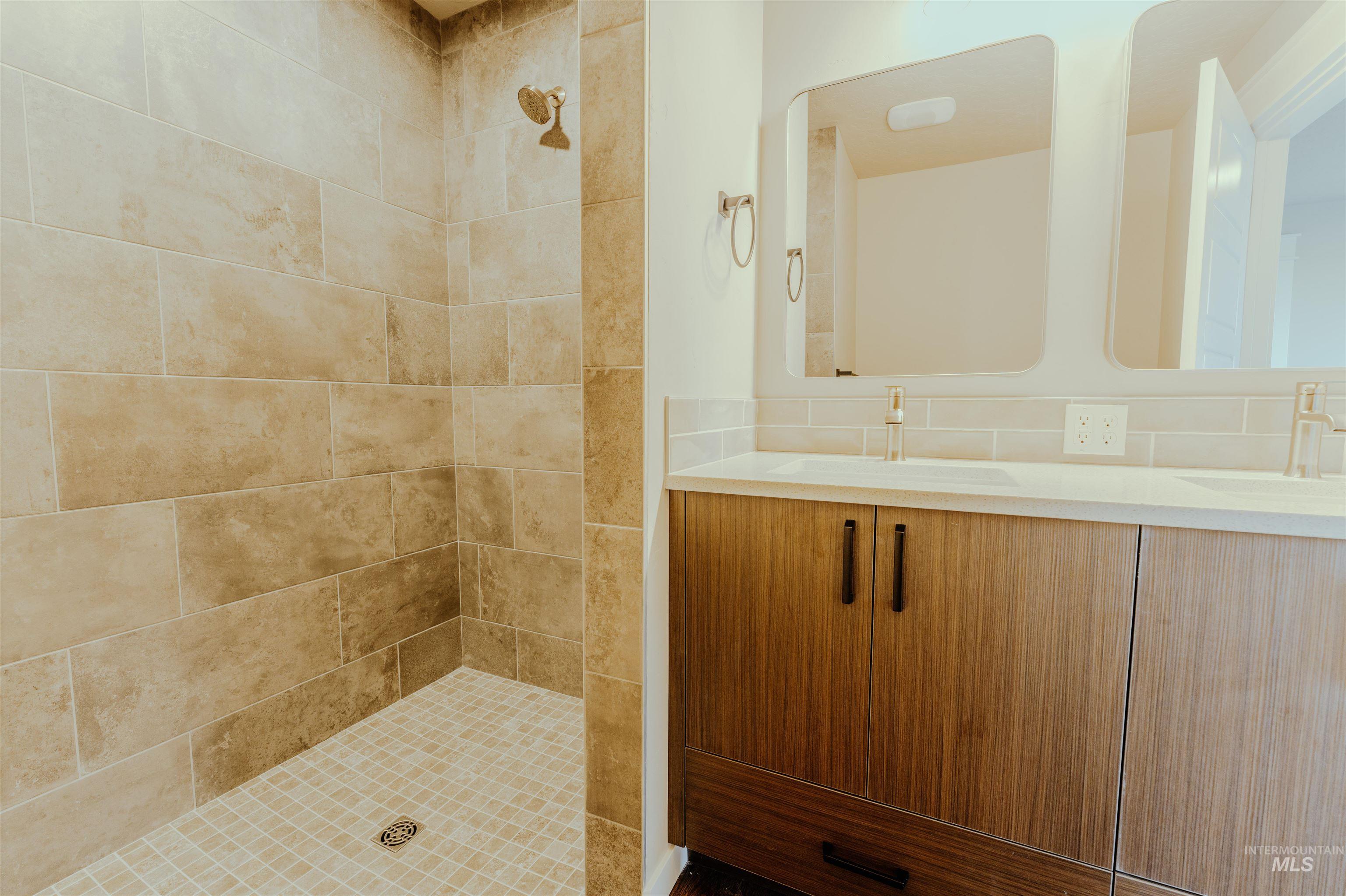Full bathroom featuring double vanity and tiled shower