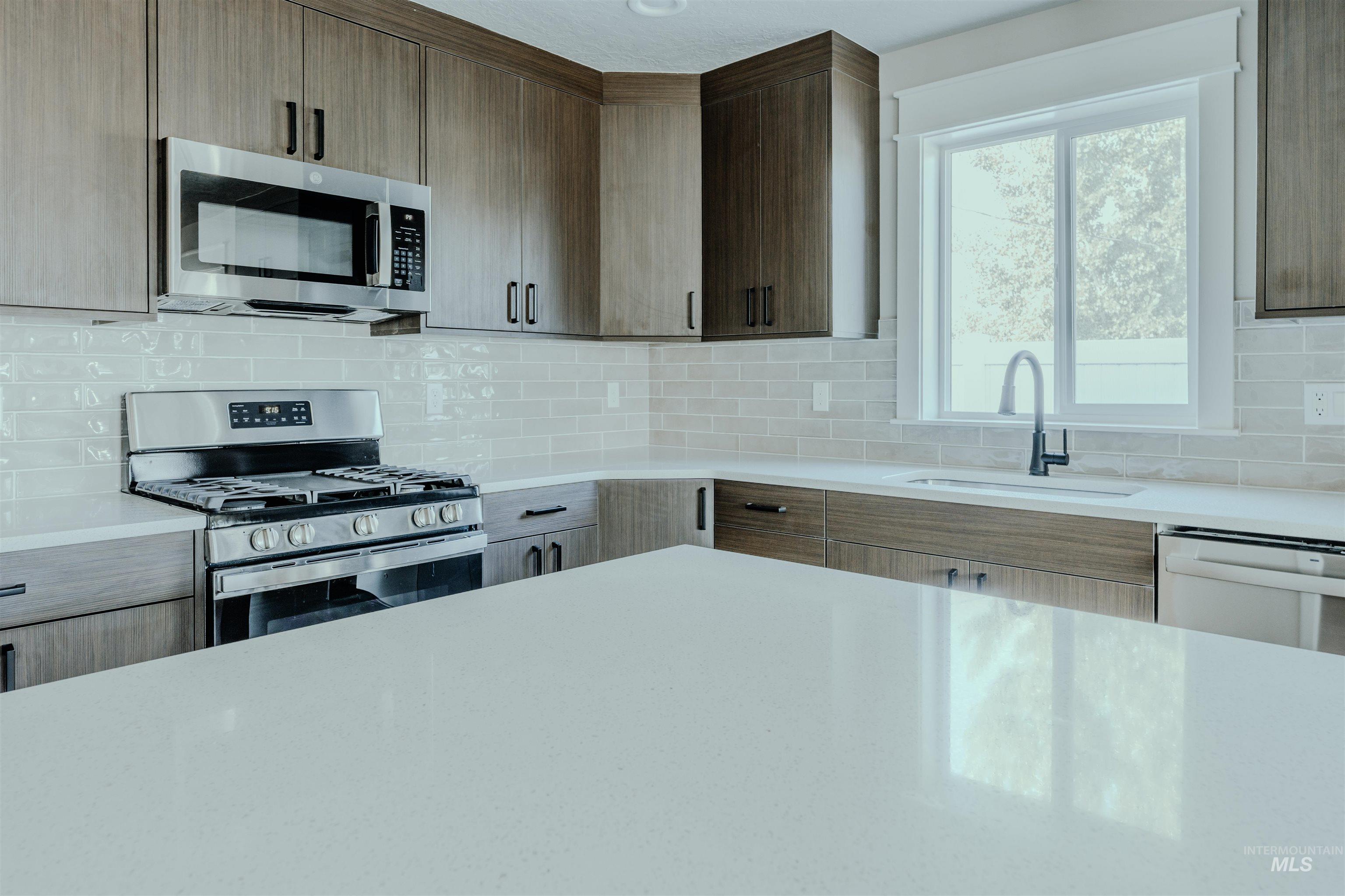 Kitchen with appliances with stainless steel finishes, tasteful backsplash, light stone counters, and modern cabinets
