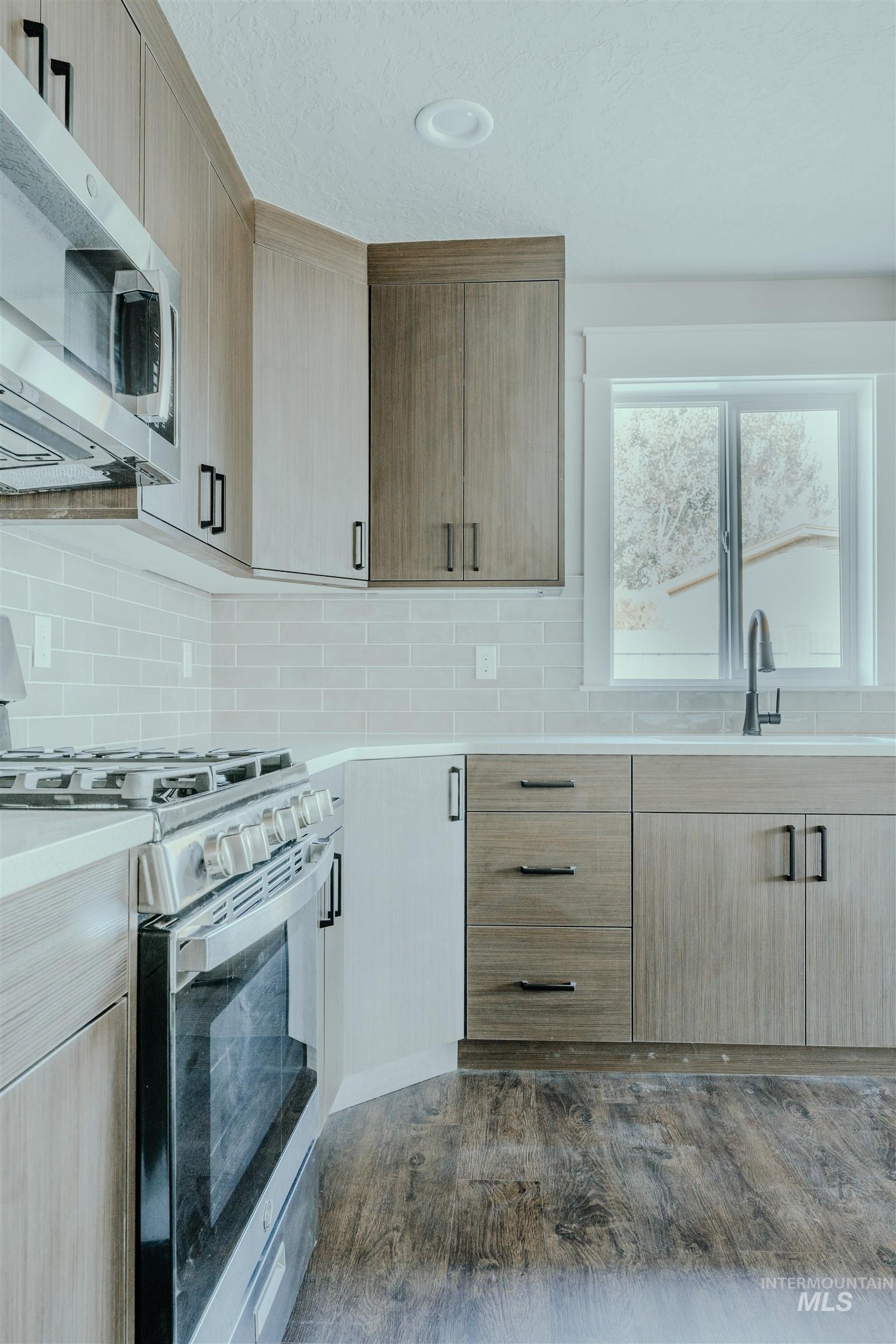 Kitchen with stainless steel appliances, light brown cabinetry, dark wood finished floors, and tasteful backsplash