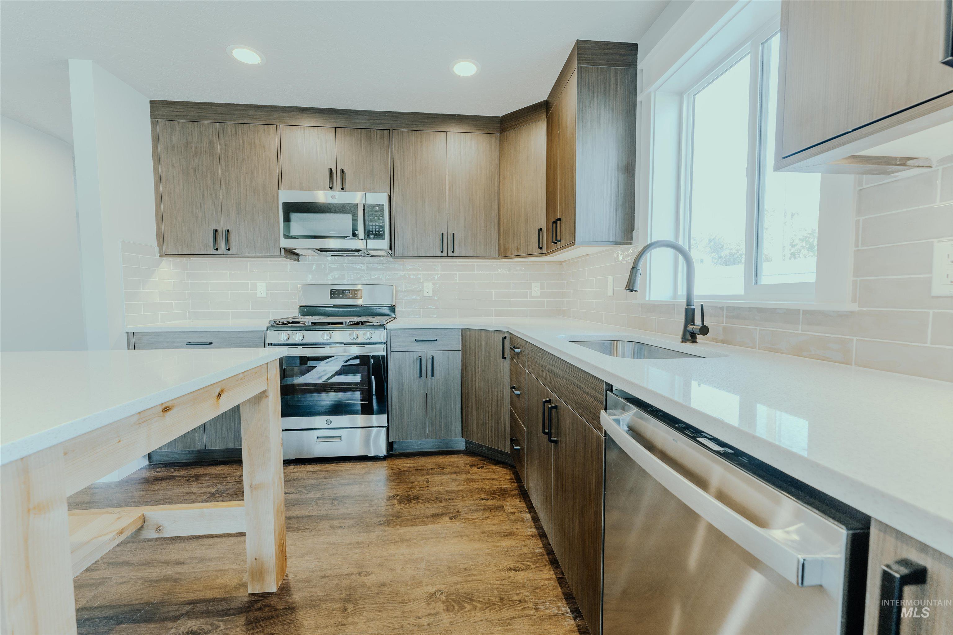 Kitchen with light stone countertops, decorative backsplash, stainless steel appliances, light wood finished floors, and recessed lighting