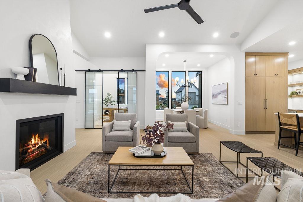 Living area with a barn door, a chandelier, light wood-type flooring, a glass covered fireplace, and recessed lighting