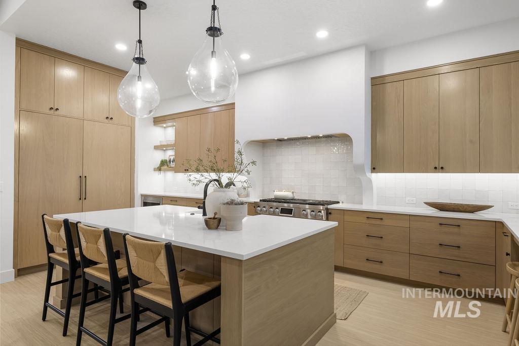 Kitchen with open shelves, modern cabinets, light brown cabinets, pendant lighting, and a breakfast bar