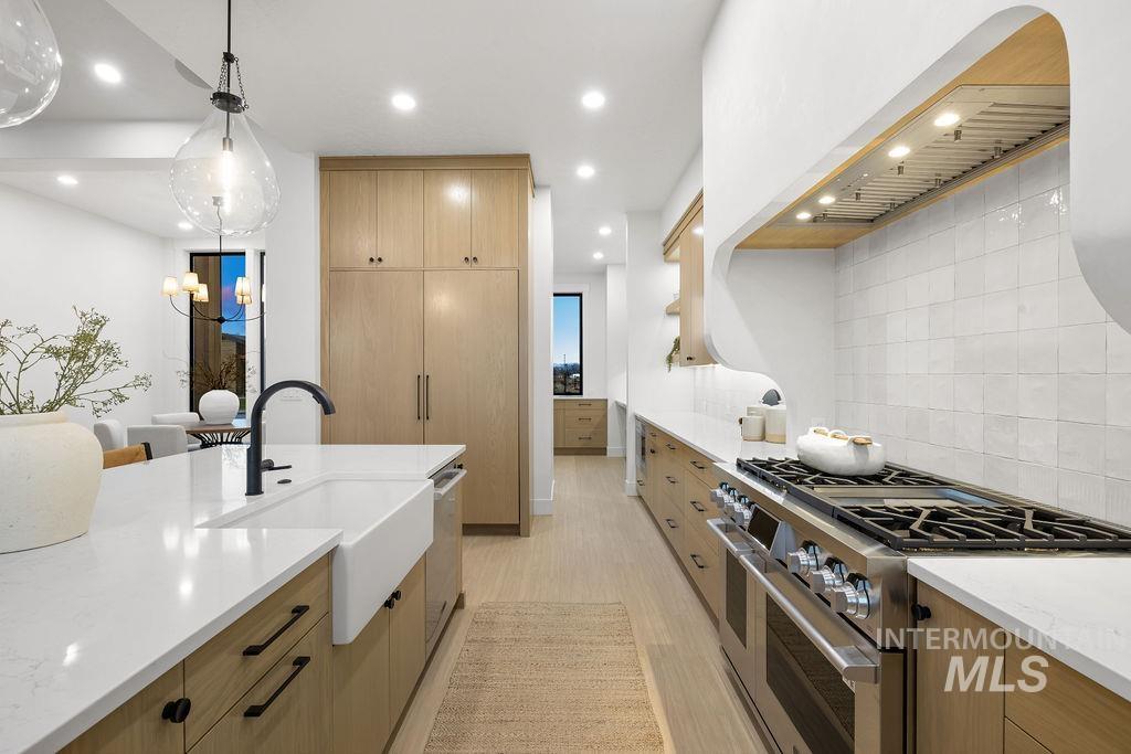 Kitchen with stainless steel appliances, modern cabinets, tasteful backsplash, light stone countertops, and pendant lighting