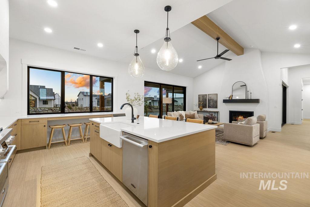 Kitchen featuring a fireplace, light brown cabinets, decorative light fixtures, light wood-style floors, and a center island with sink