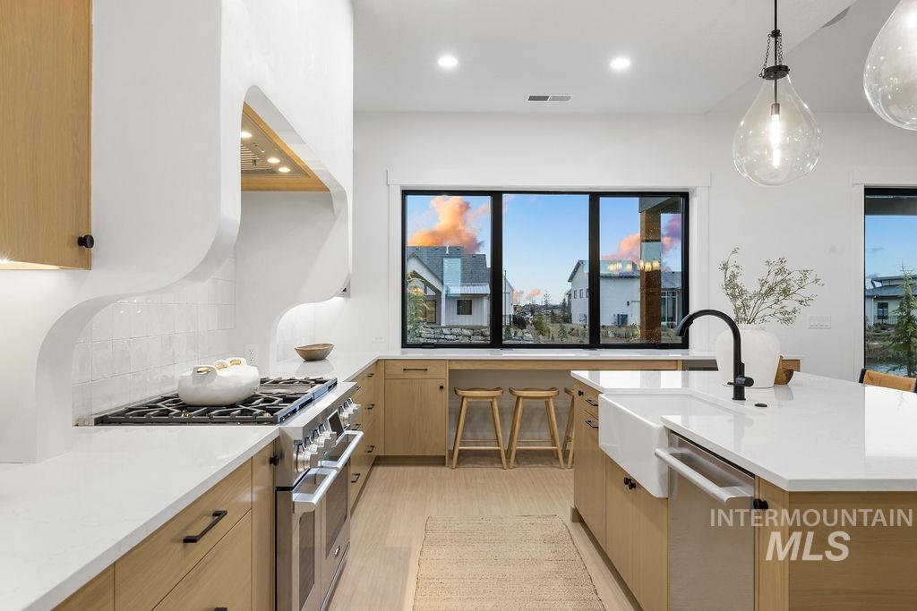 Kitchen featuring appliances with stainless steel finishes, light stone countertops, pendant lighting, modern cabinets, and light wood finished floors