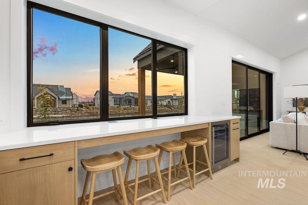 Kitchen featuring beverage cooler, a kitchen breakfast bar, light wood finished floors, light brown cabinets, and lofted ceiling