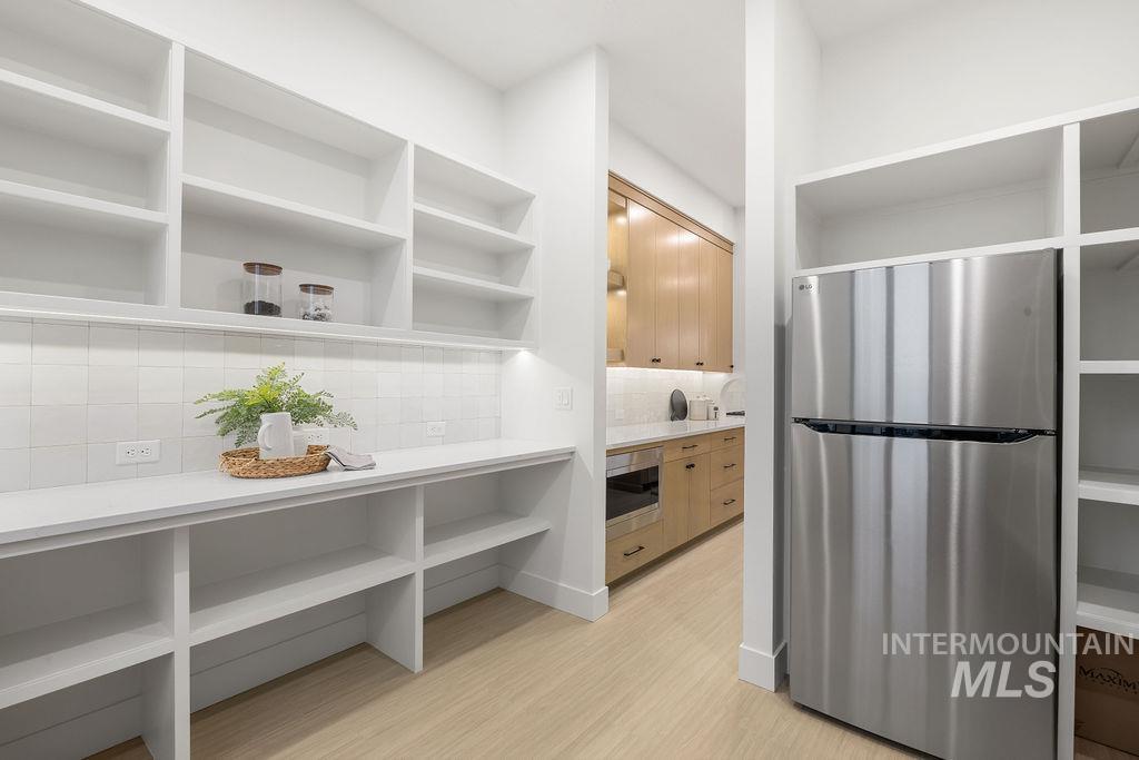 Bathroom featuring a stall shower, light wood-type flooring, decorative backsplash, vanity, and a closet