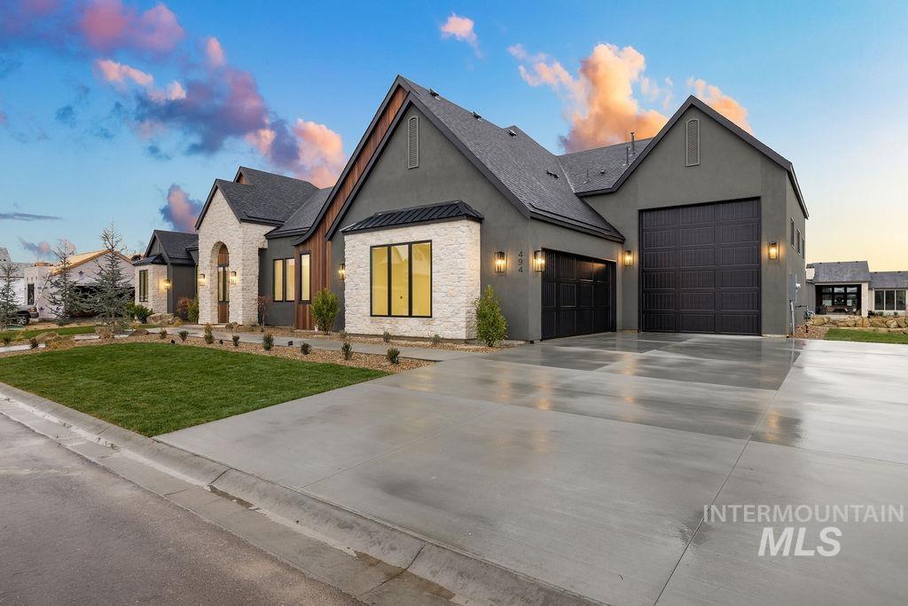View of front of house featuring stone siding, a standing seam roof, stucco siding, an attached garage, and concrete driveway