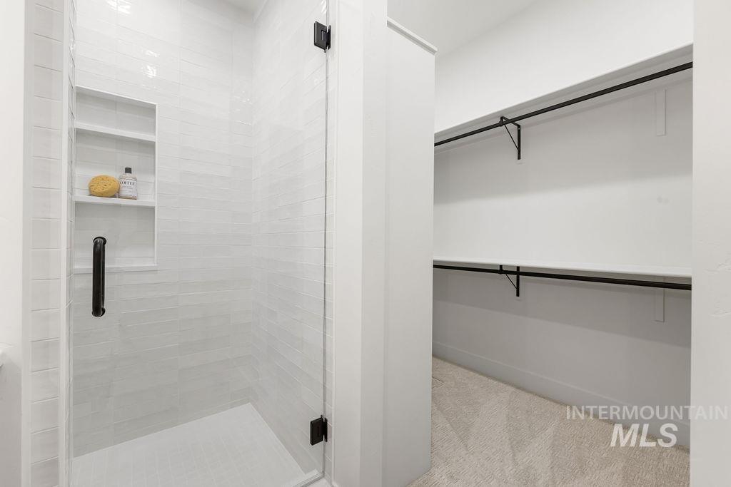 Full bathroom featuring a stall shower, a spacious closet, and light colored carpet