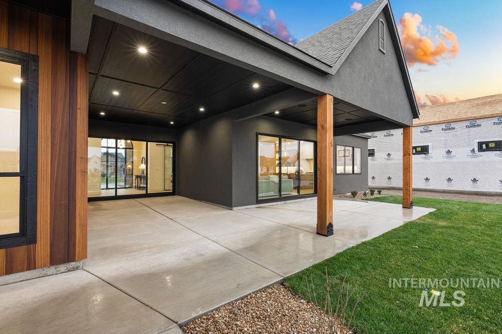 Back of property at dusk with a patio area, stucco siding, and a lawn