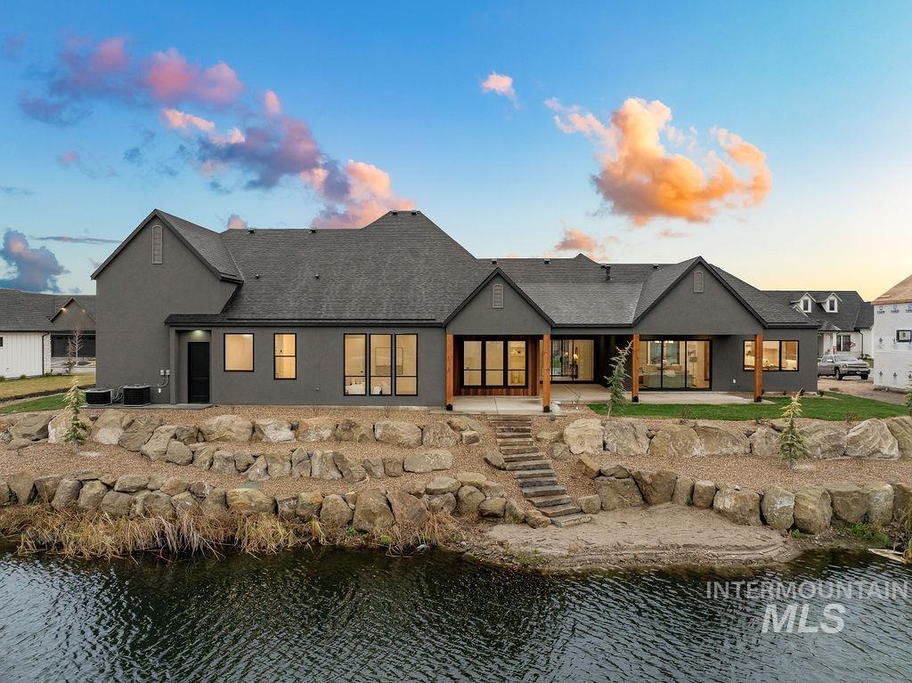 Back of property featuring a patio, a water view, stucco siding, and roof with shingles