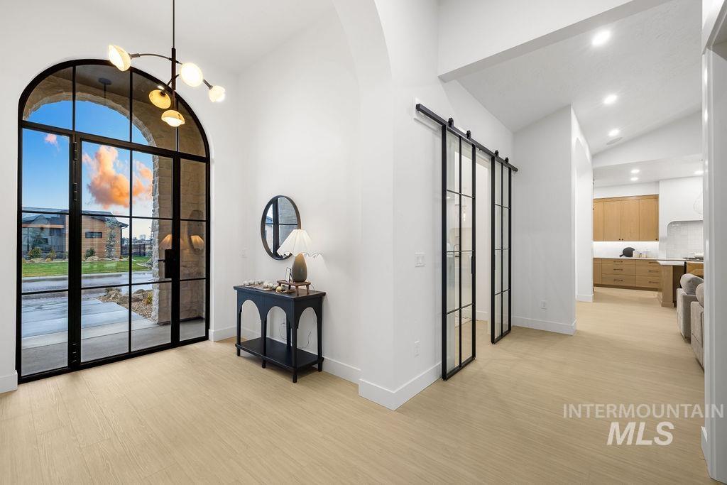 Foyer entrance with a barn door, vaulted ceiling, a chandelier, light wood-style flooring, and arched walkways