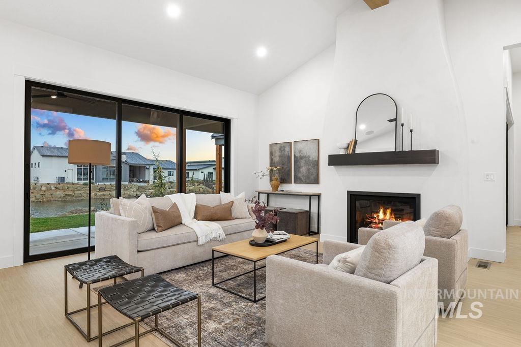 Living area with a glass covered fireplace, light wood finished floors, high vaulted ceiling, and recessed lighting