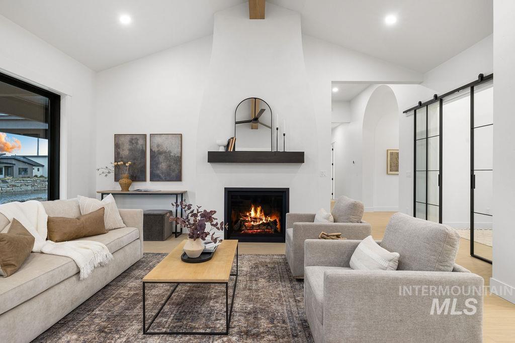 Living room featuring a barn door, a warm lit fireplace, arched walkways, wood finished floors, and recessed lighting