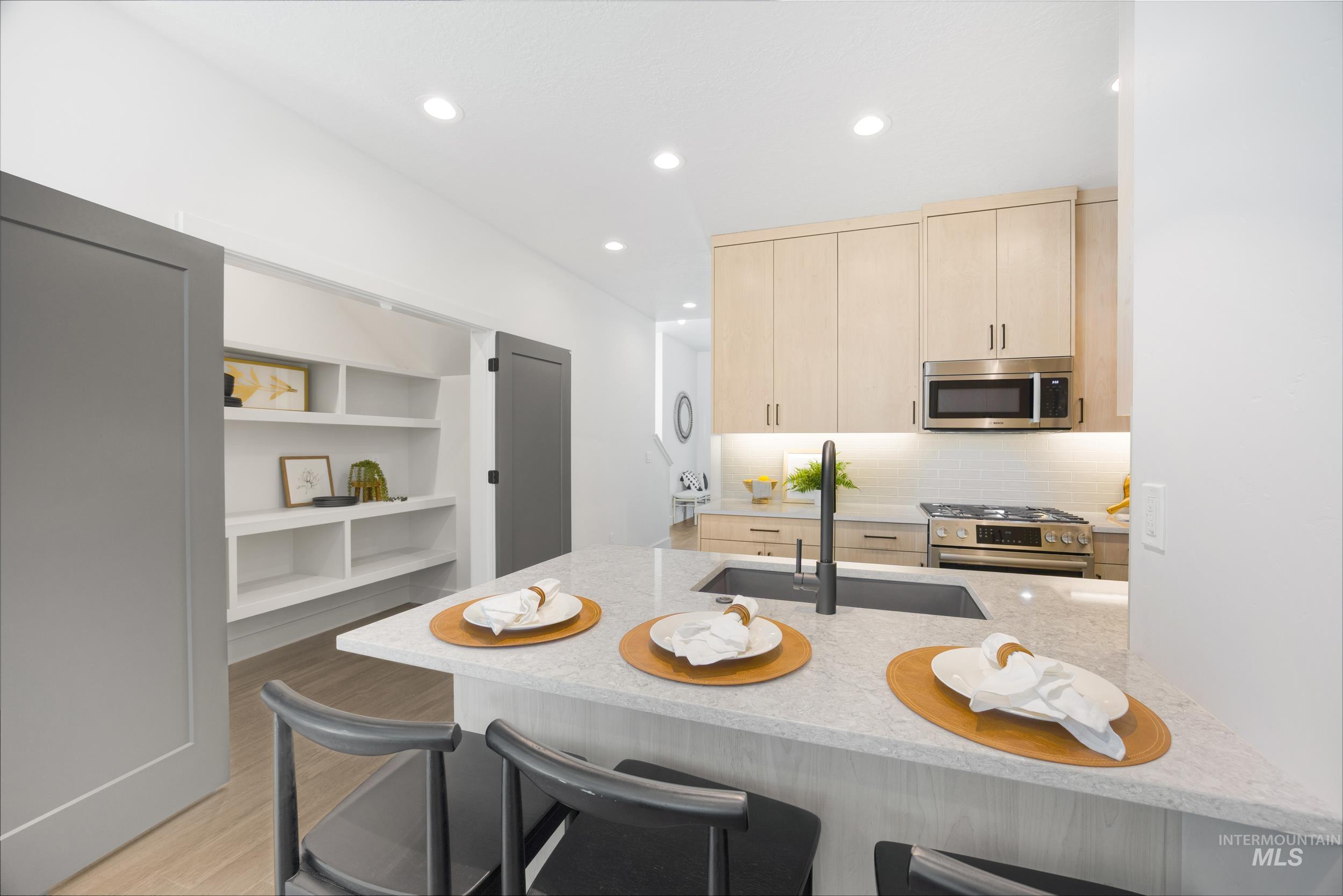Kitchen with light brown cabinets, light stone counters, backsplash, recessed lighting, and a peninsula