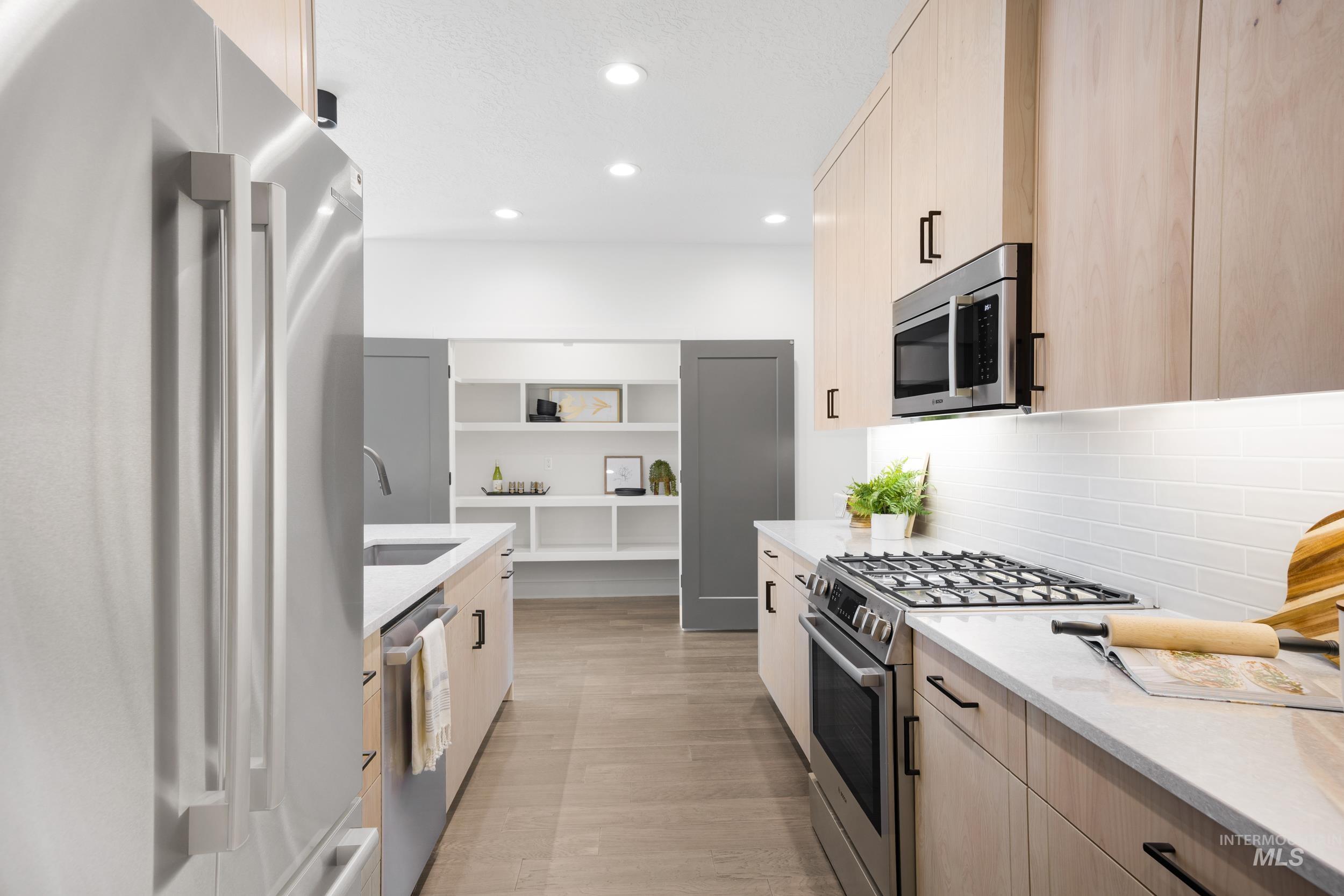 Kitchen with light brown cabinetry, appliances with stainless steel finishes, light stone counters, recessed lighting, and modern cabinets