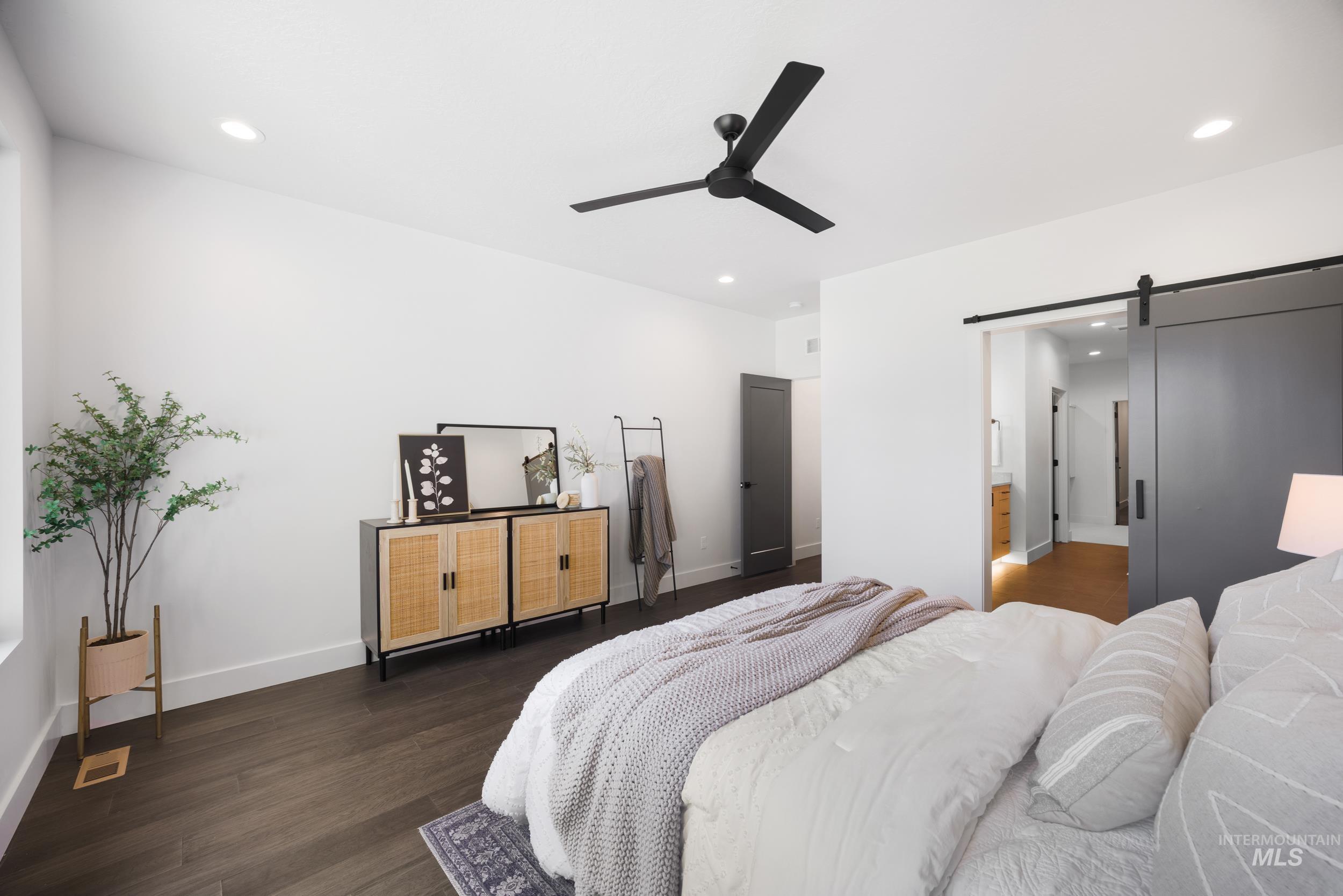 Bedroom with a barn door, dark wood-type flooring, recessed lighting, a ceiling fan, and ensuite bath