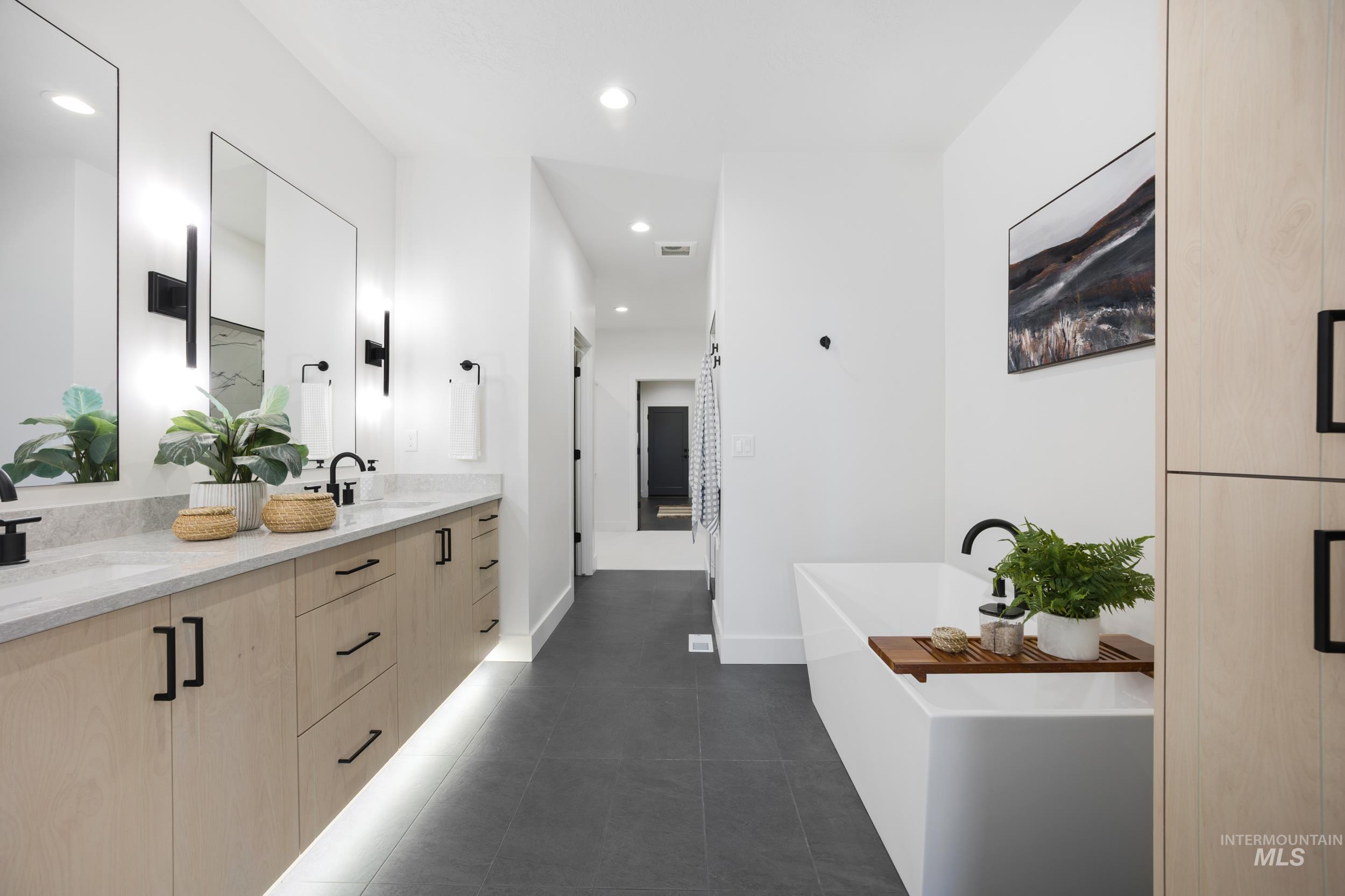 Bathroom with a freestanding tub, double vanity, dark tile patterned floors, and recessed lighting