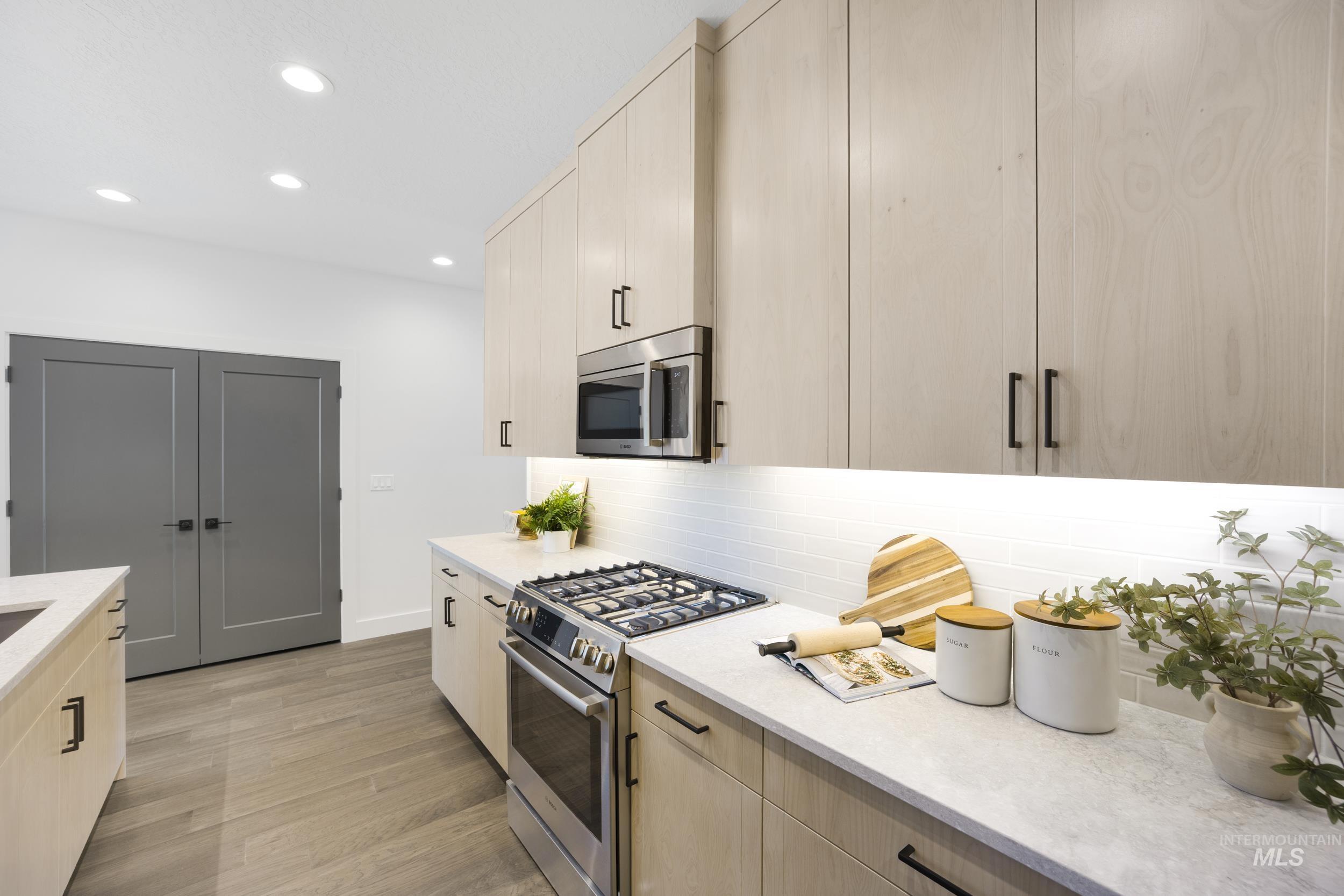 Kitchen with light brown cabinets, appliances with stainless steel finishes, light stone counters, recessed lighting, and tasteful backsplash