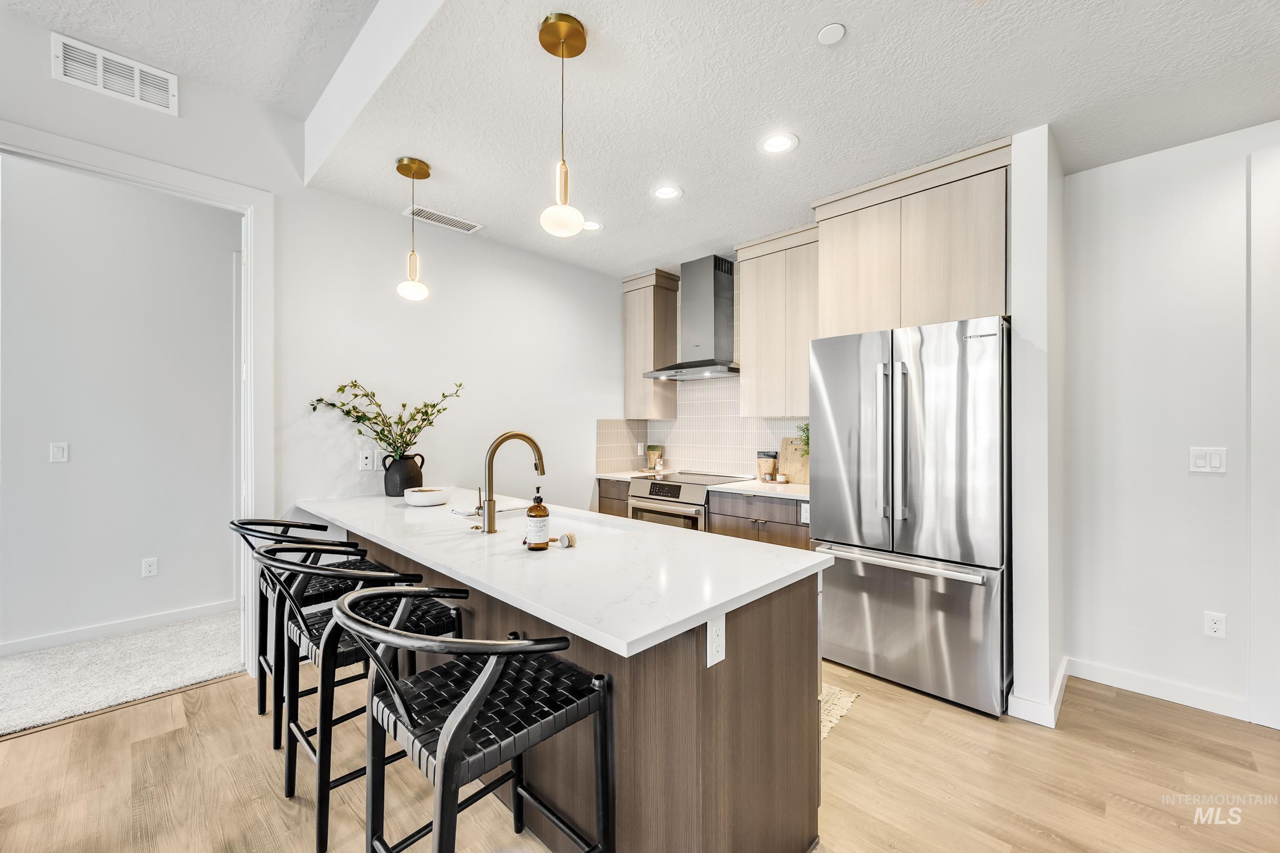 Kitchen featuring appliances with stainless steel finishes, pendant lighting, a kitchen bar, backsplash, and light stone countertops