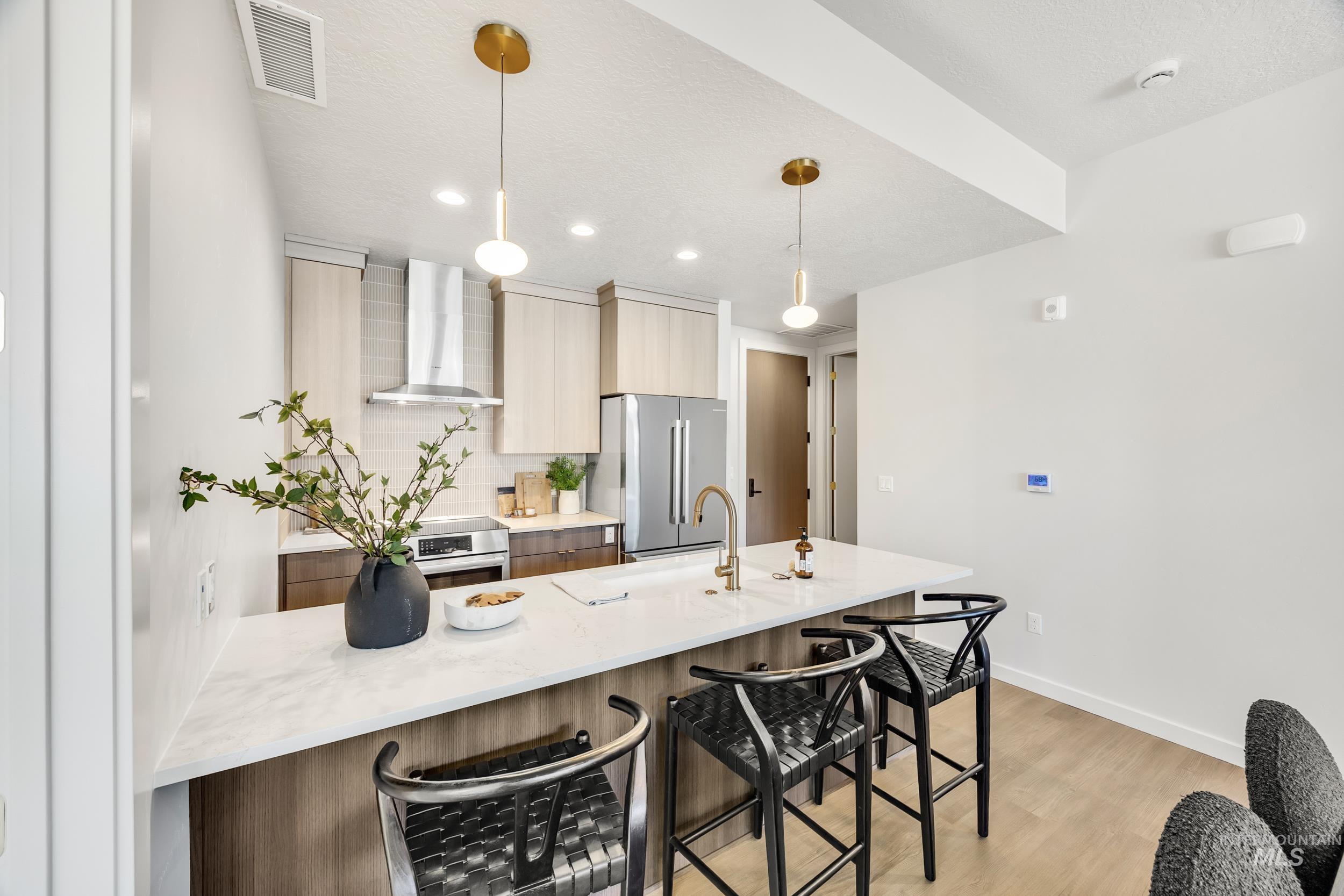 Kitchen with modern cabinets, light stone countertops, tasteful backsplash, wall chimney range hood, and a breakfast bar area