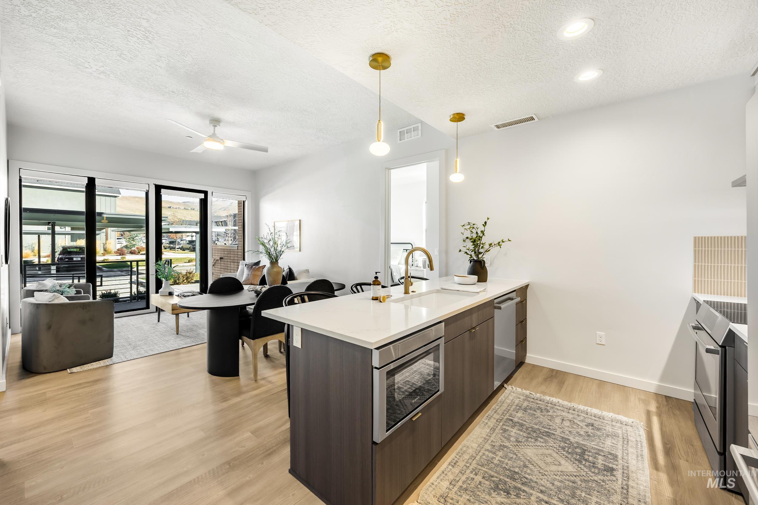 Kitchen with a peninsula, light wood-style flooring, a textured ceiling, open floor plan, and appliances with stainless steel finishes
