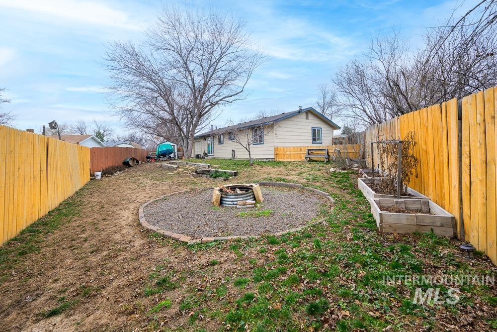 Fenced backyard featuring a garden, a patio area, and a fire pit