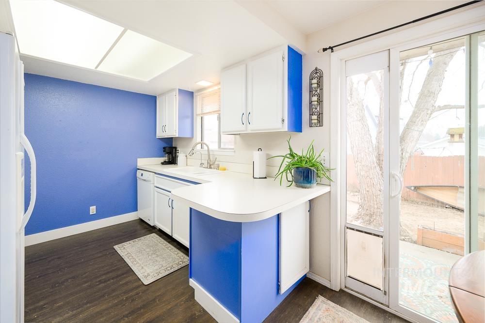Kitchen featuring white appliances, white cabinets, light countertops, and dark wood-style flooring