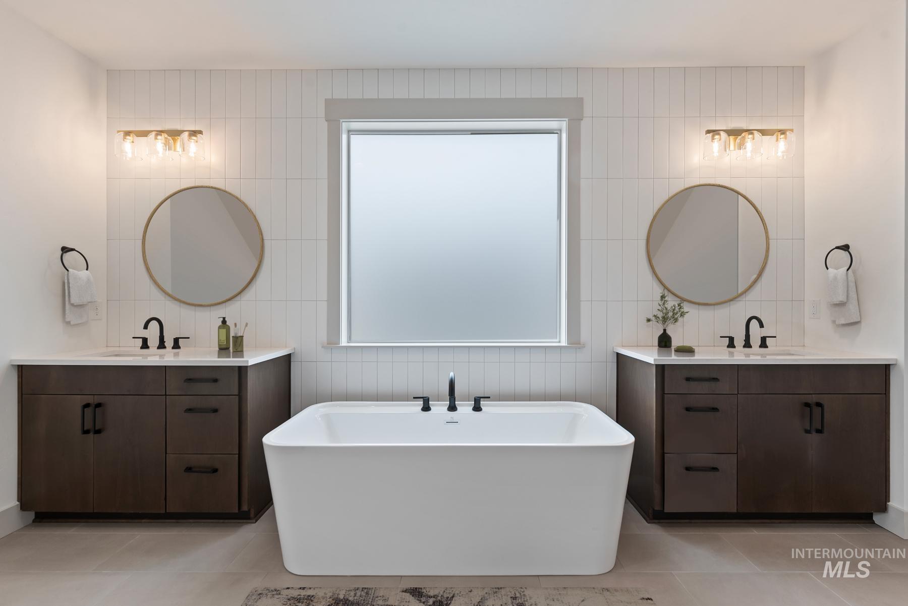 Bathroom with a freestanding bath, tile walls, light tile patterned floors, and two vanities