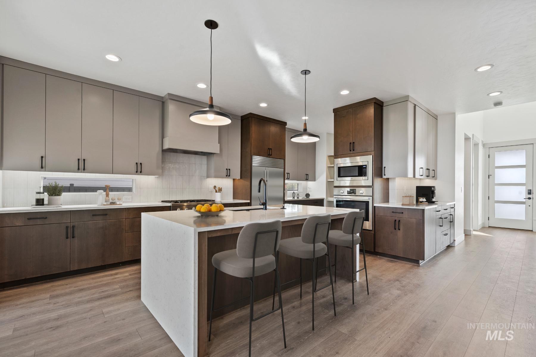 Kitchen with a kitchen breakfast bar, backsplash, built in appliances, light stone counters, and custom exhaust hood