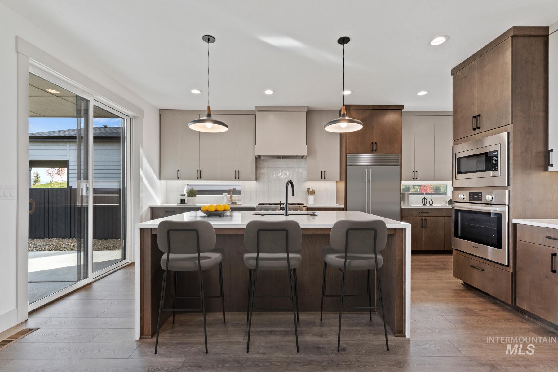Kitchen with built in appliances, a center island with sink, hanging light fixtures, a breakfast bar, and recessed lighting