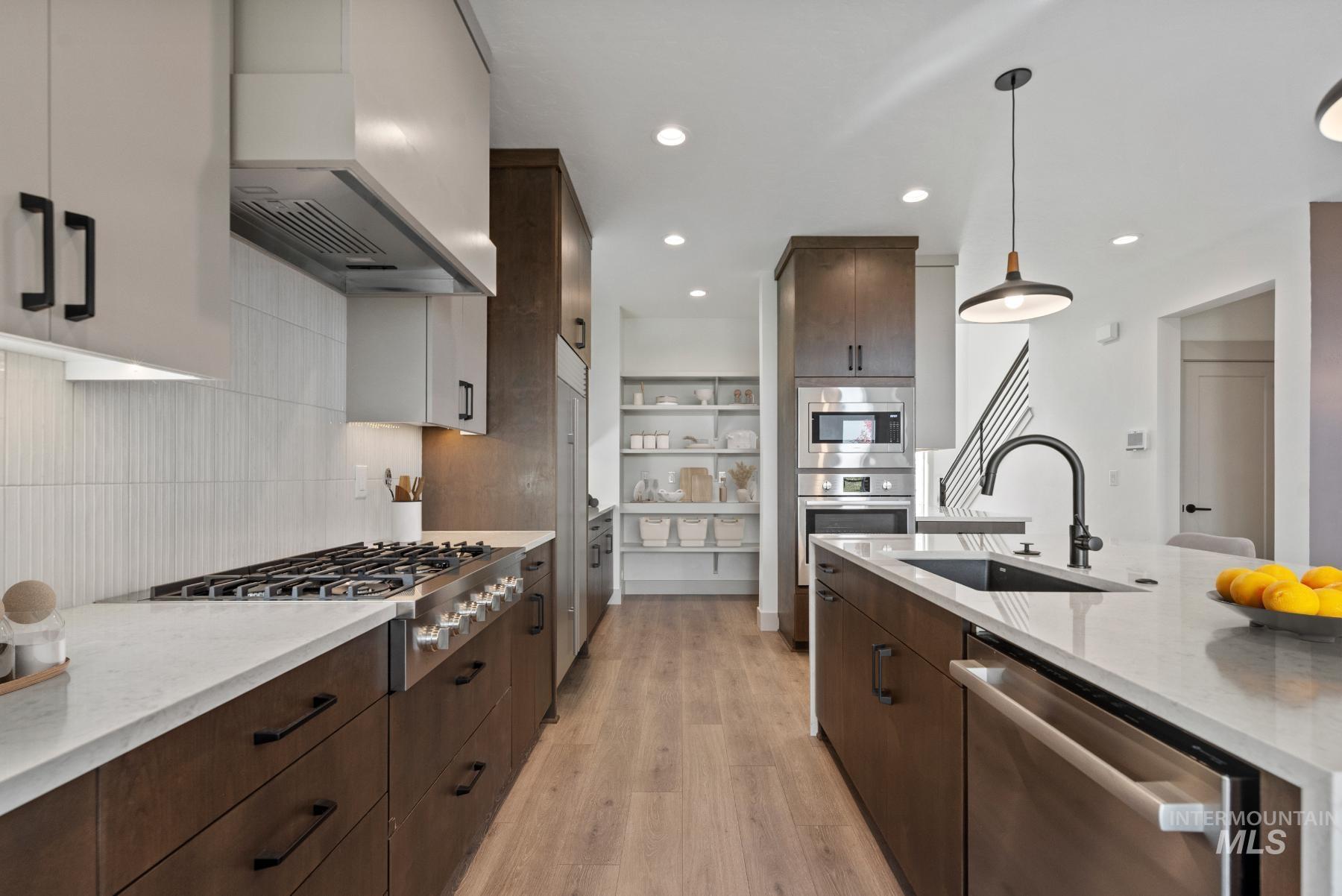 Kitchen featuring dark brown cabinetry, light stone counters, wall chimney exhaust hood, appliances with stainless steel finishes, and light wood-type flooring