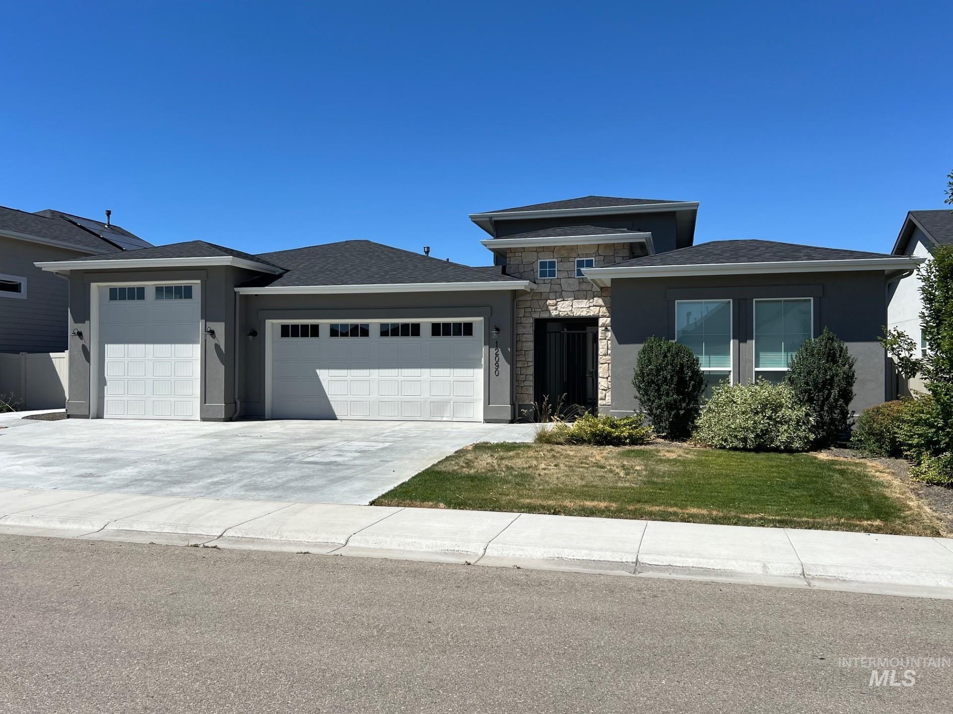 Prairie-style house with an attached garage, stone siding, stucco siding, driveway, and a front lawn