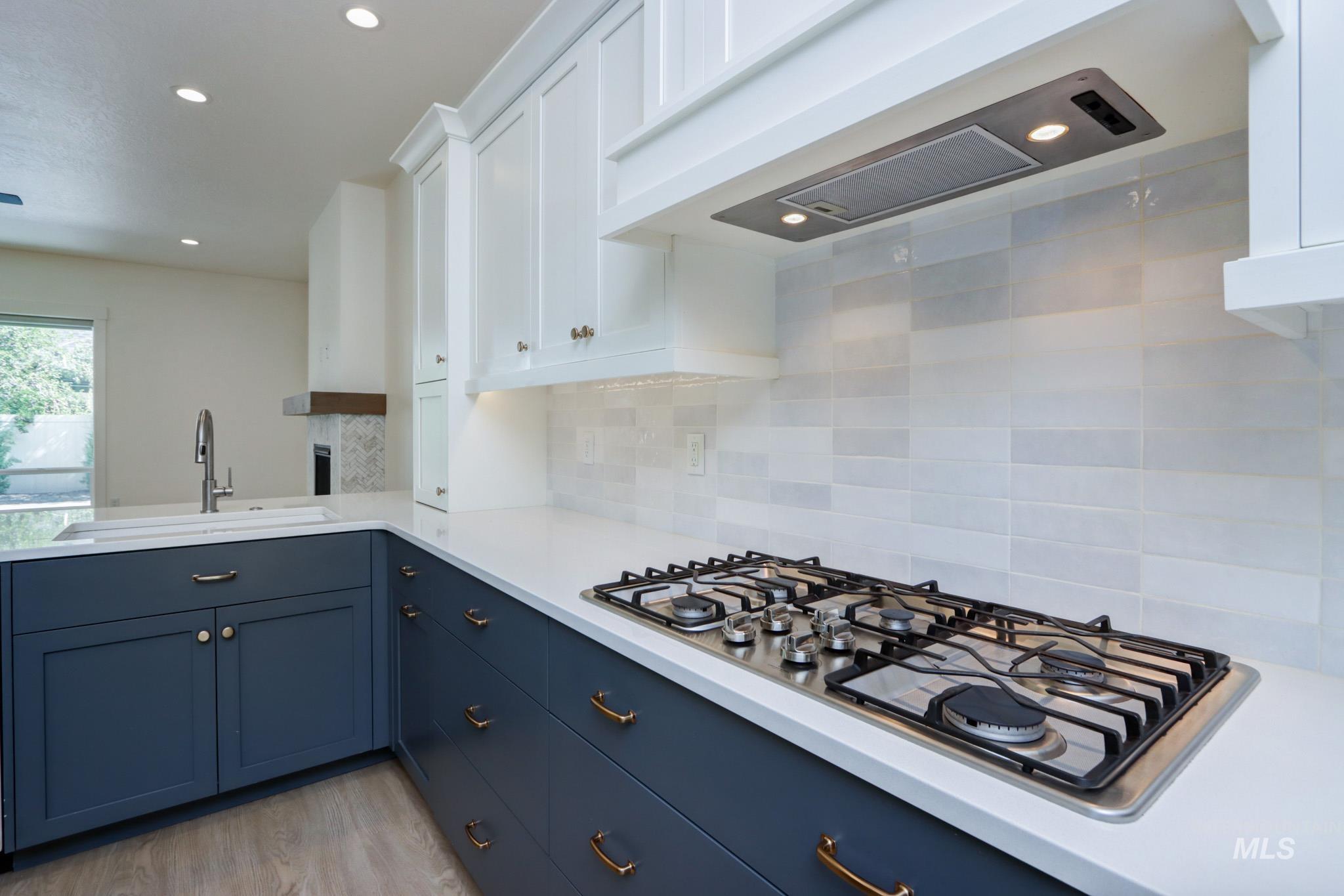Kitchen featuring ventilation hood, stainless steel gas cooktop, backsplash, light countertops, and blue cabinetry