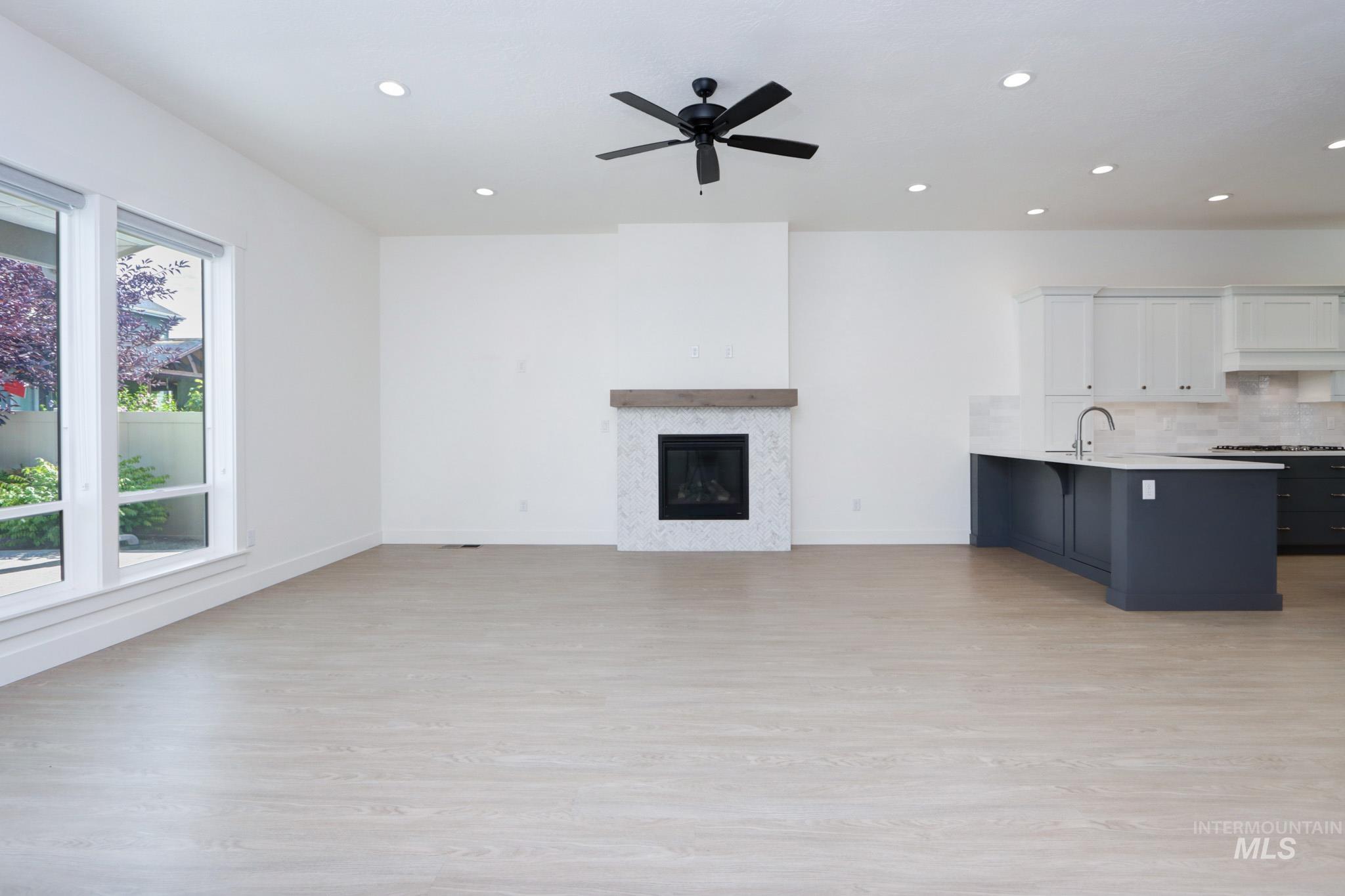 Unfurnished living room featuring light wood-style flooring, a glass covered fireplace, a ceiling fan, and recessed lighting