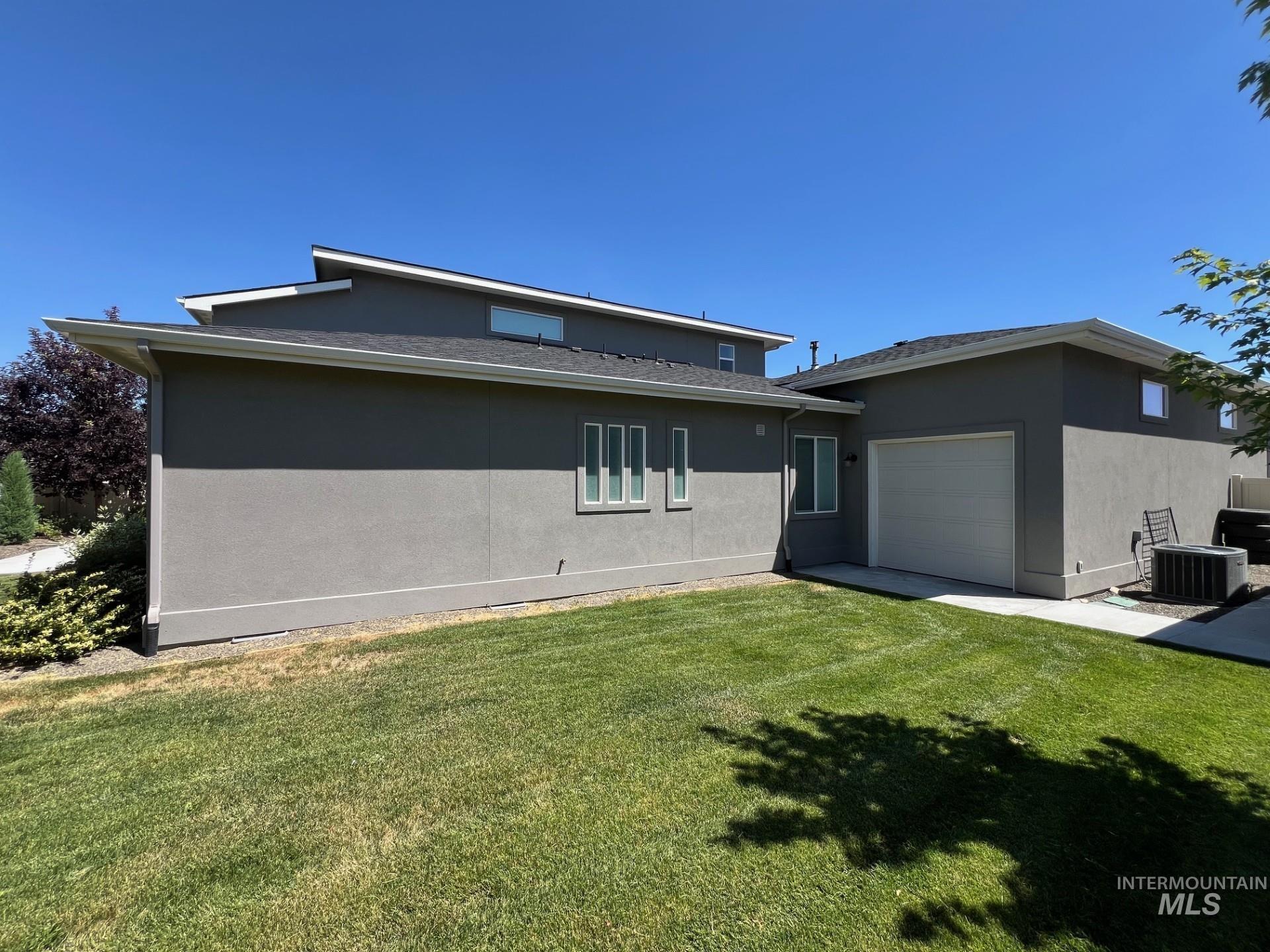 Back of property with an attached garage, a yard, and stucco siding