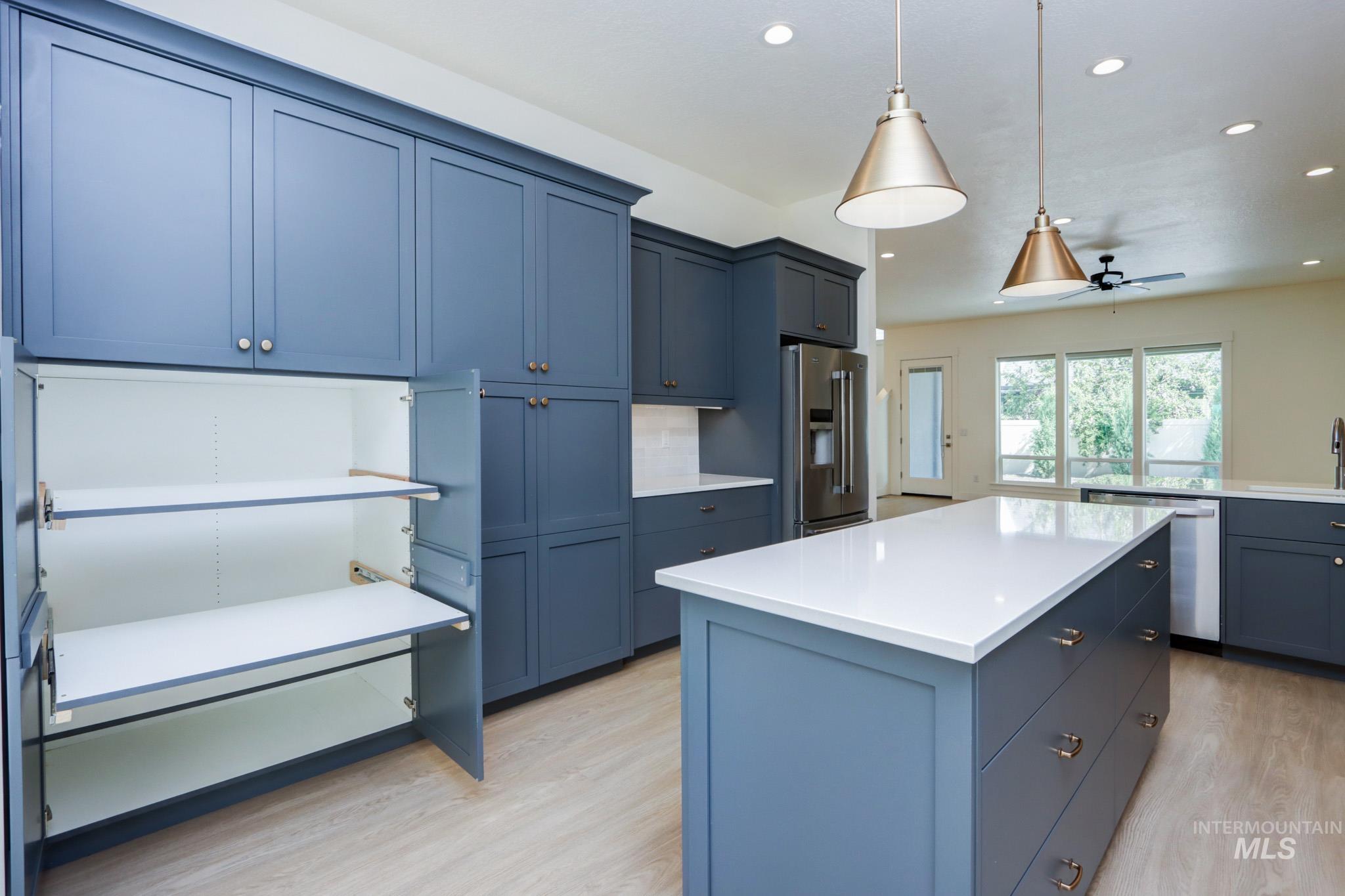 Kitchen with light wood finished floors, a center island, appliances with stainless steel finishes, light countertops, and hanging light fixtures