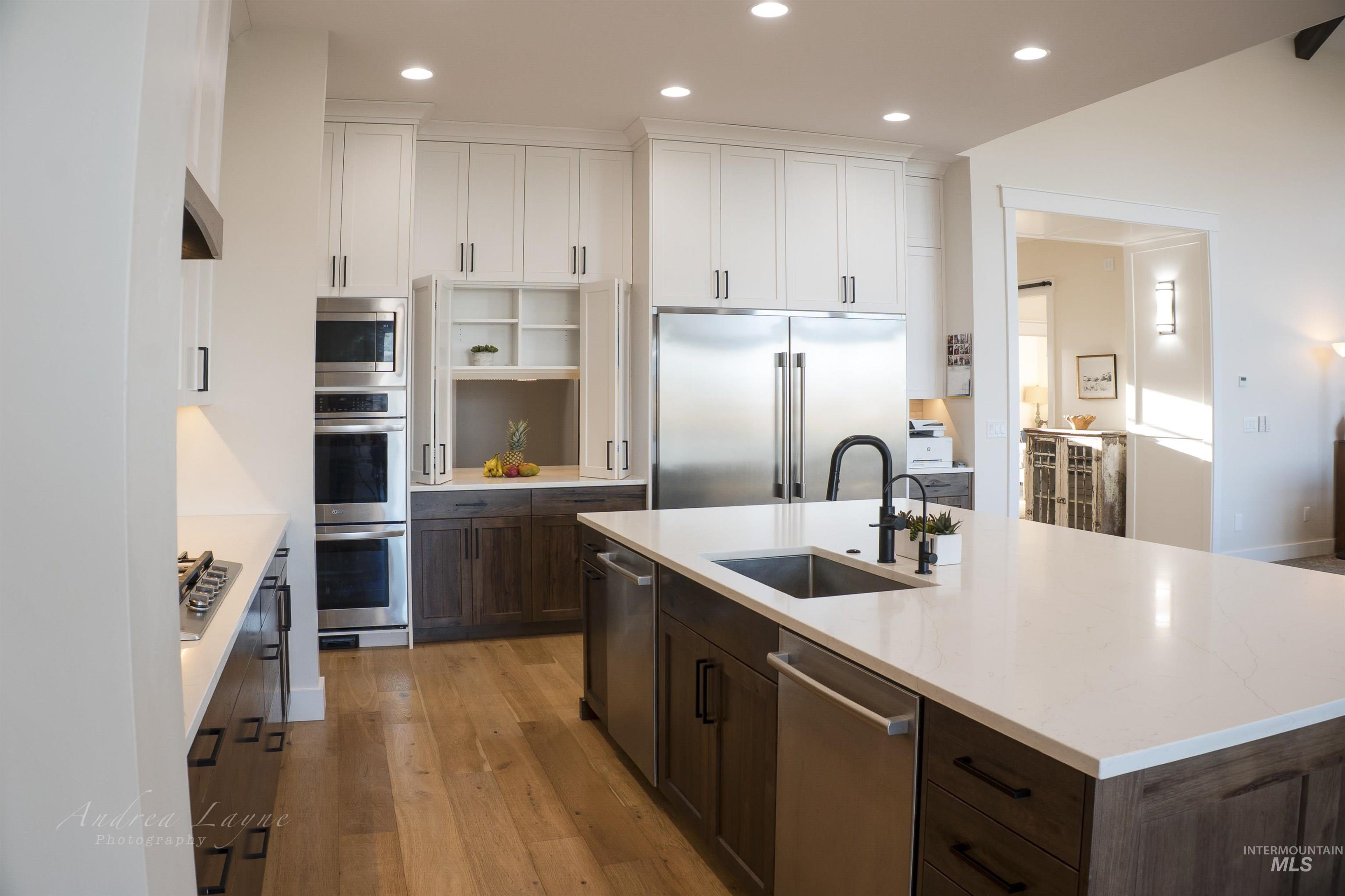 Kitchen featuring dark brown cabinets, light wood-style flooring, built in appliances, a kitchen island with sink, and recessed lighting