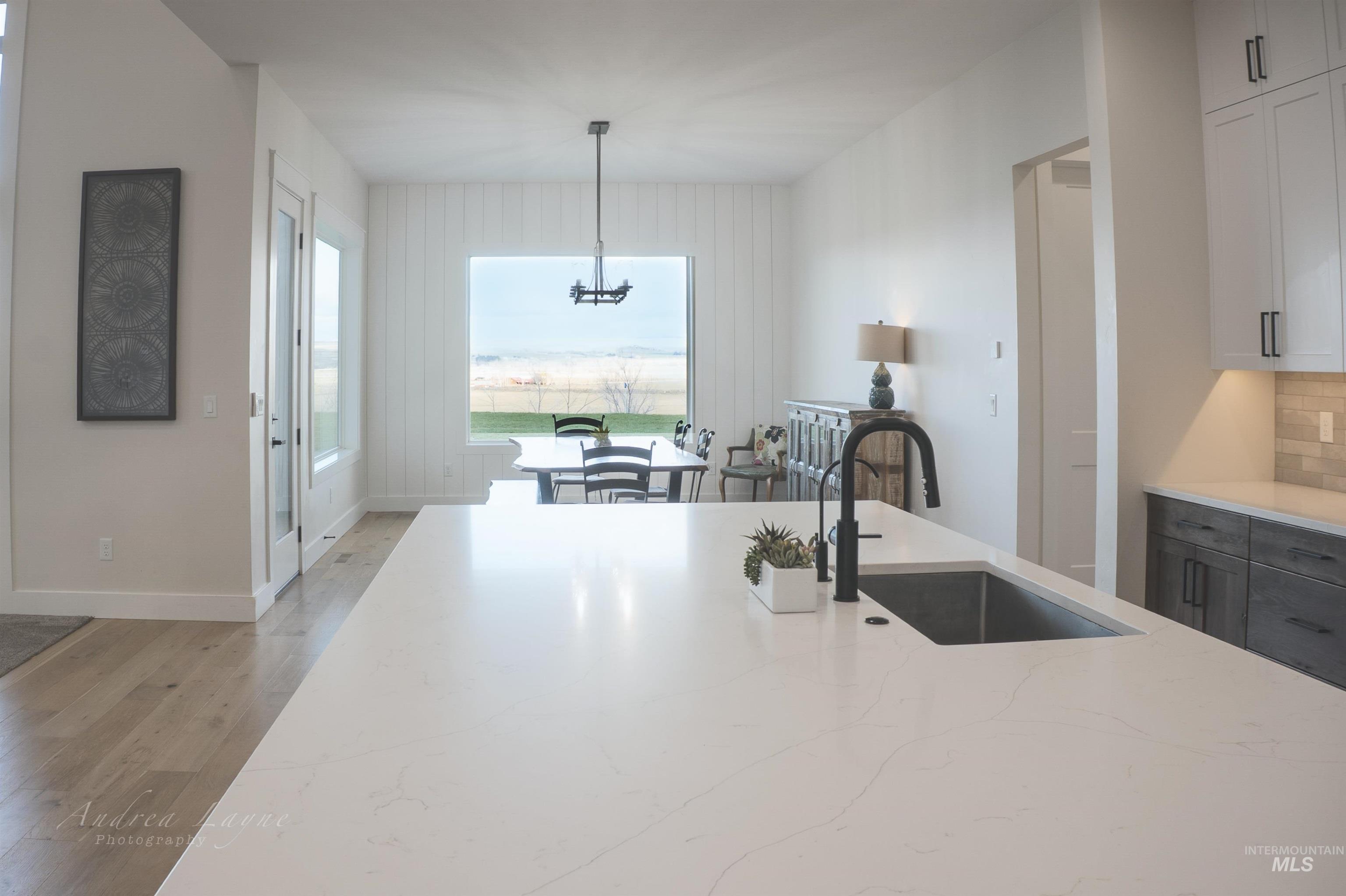 Kitchen featuring light stone countertops, light wood-type flooring, pendant lighting, and white cabinetry